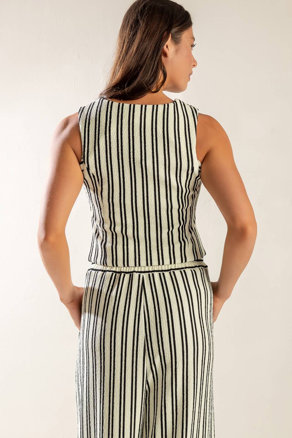 A striped black and white woven vest featuring sleeveless and front button closure.