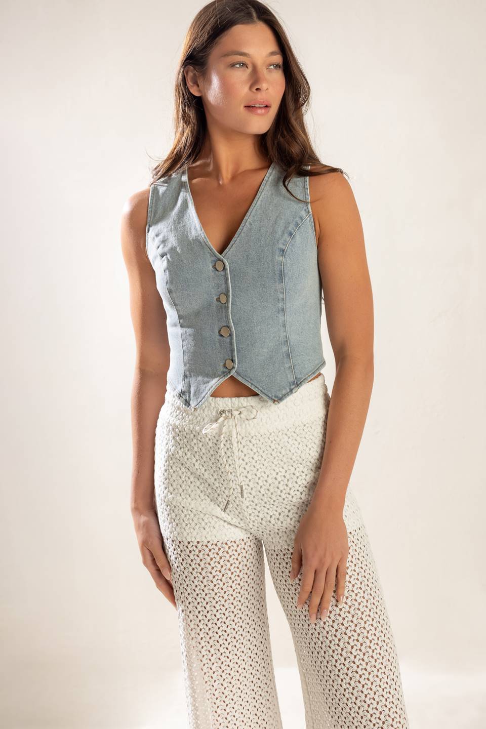 A cropped, light washed, sleeveless, denim vest with front button closure.