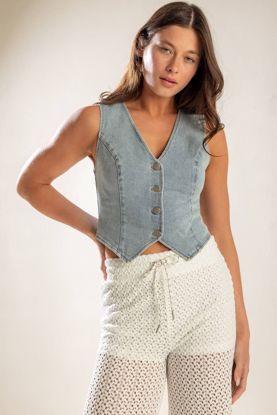 A cropped, light washed, sleeveless, denim vest with front button closure.