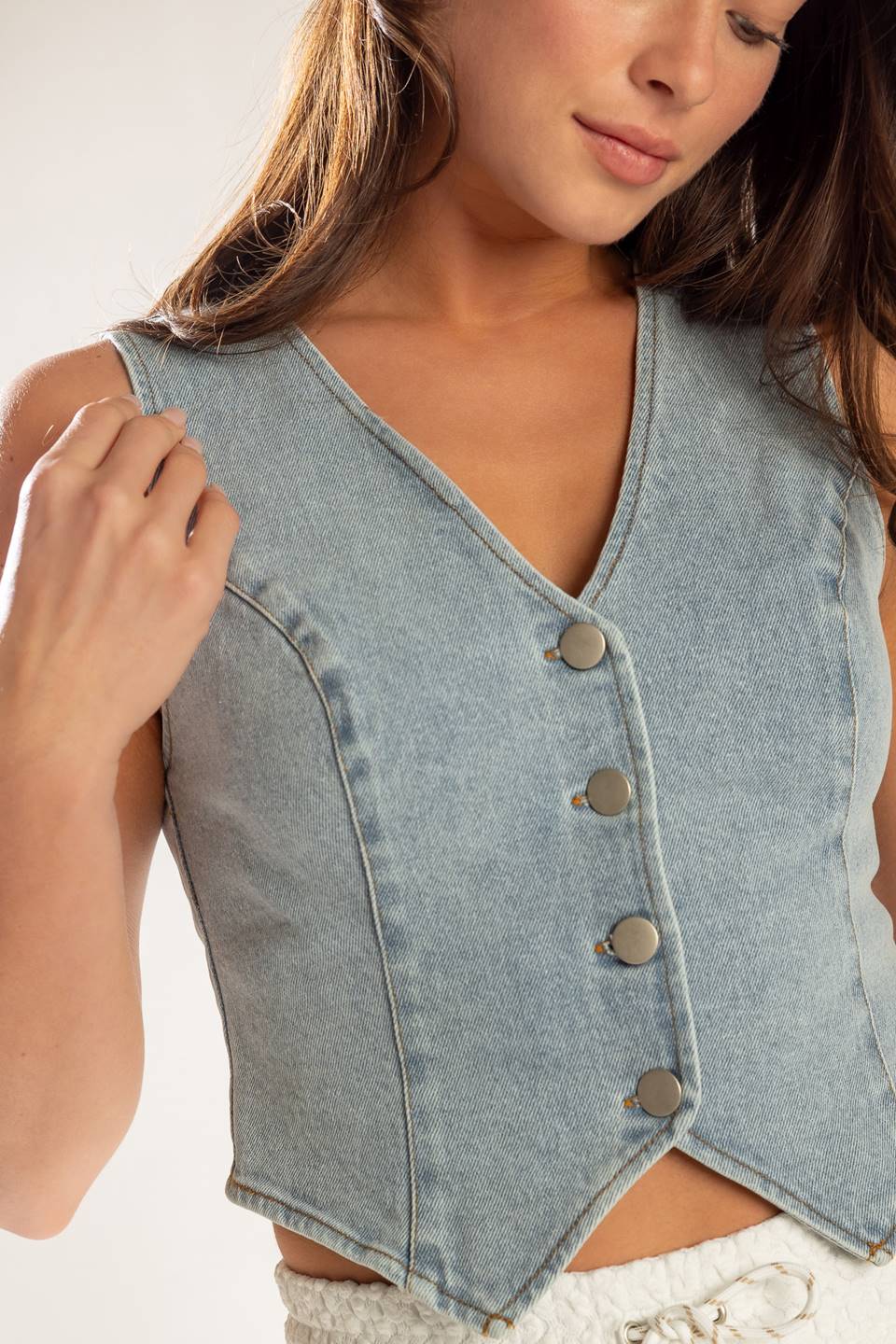 A cropped, light washed, sleeveless, denim vest with front button closure.