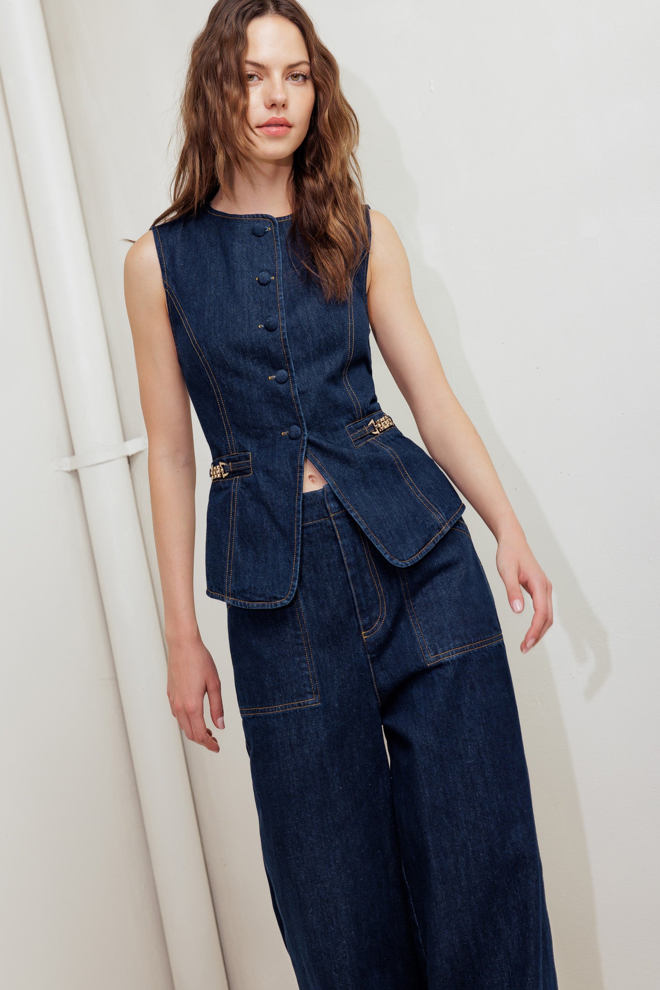 A denim vest featuring round neckline, sleeveless, front button down and hardware trim.