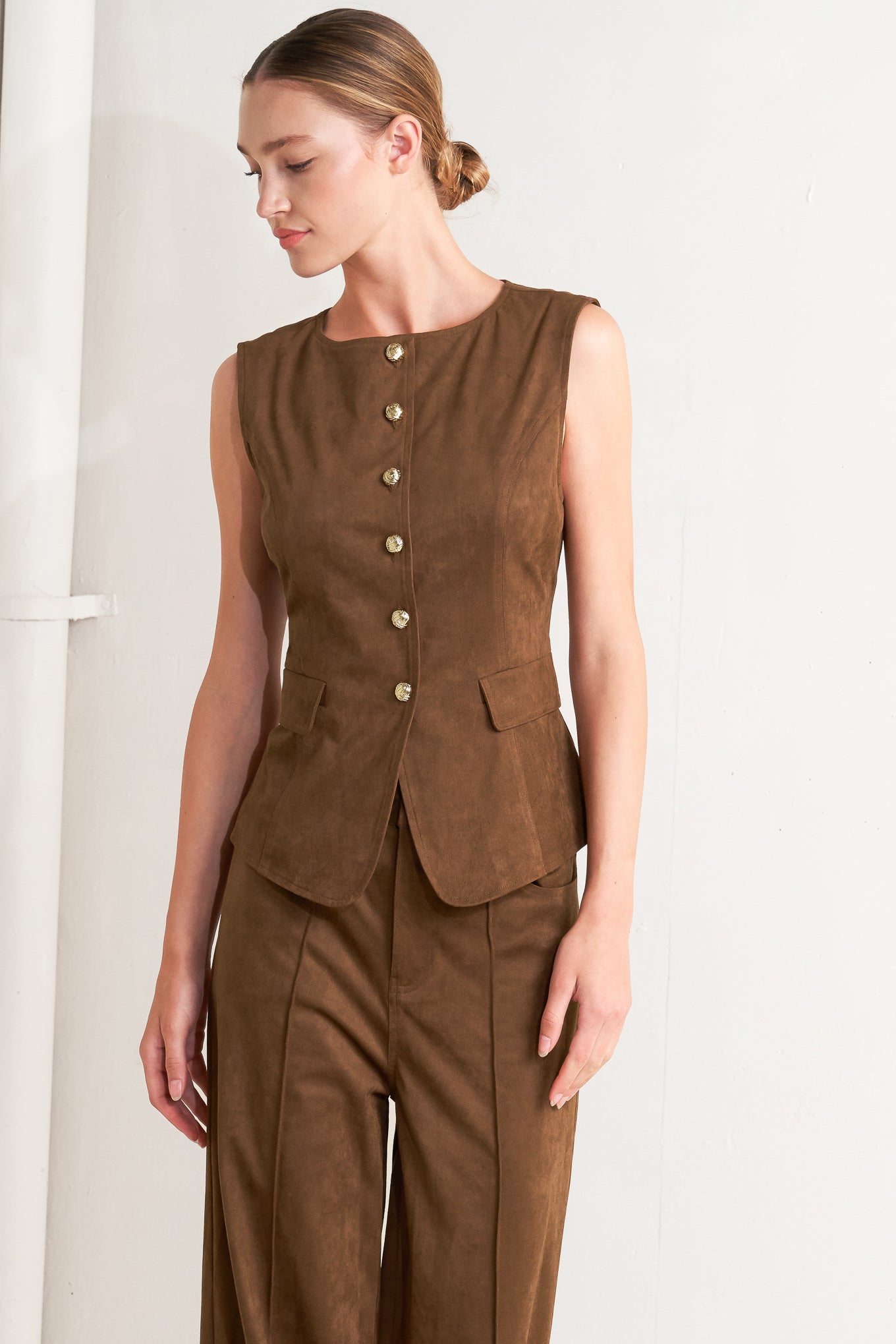 A faux suede vest featuring round neckline, sleeveless, front button closure and side pocket.