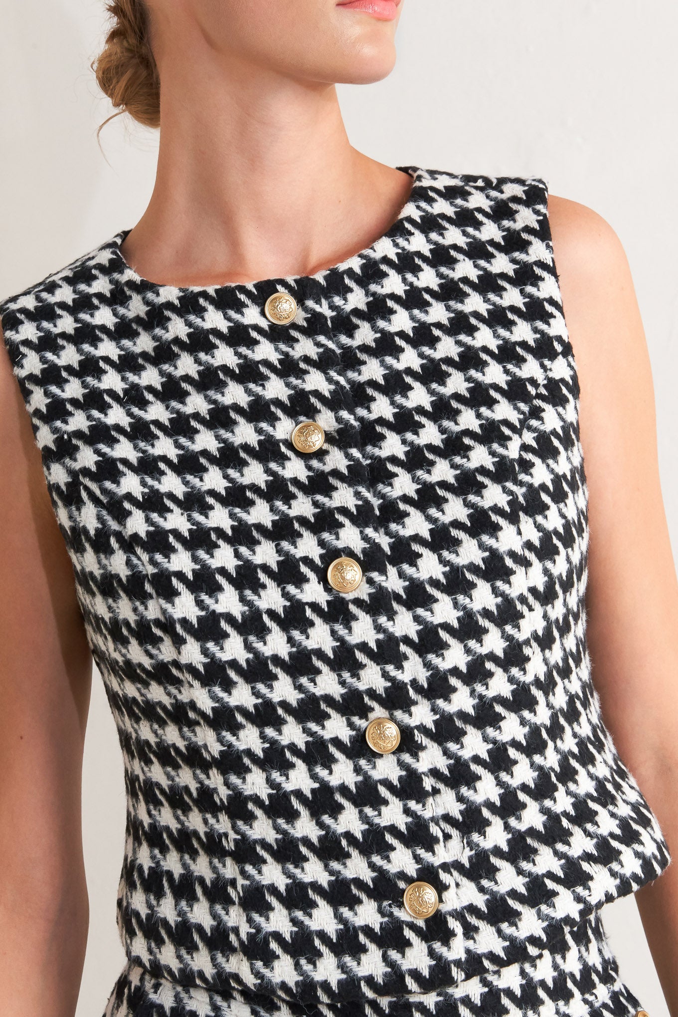 A woven houndstooth vest featuring round neckline, sleeveless and front button down.