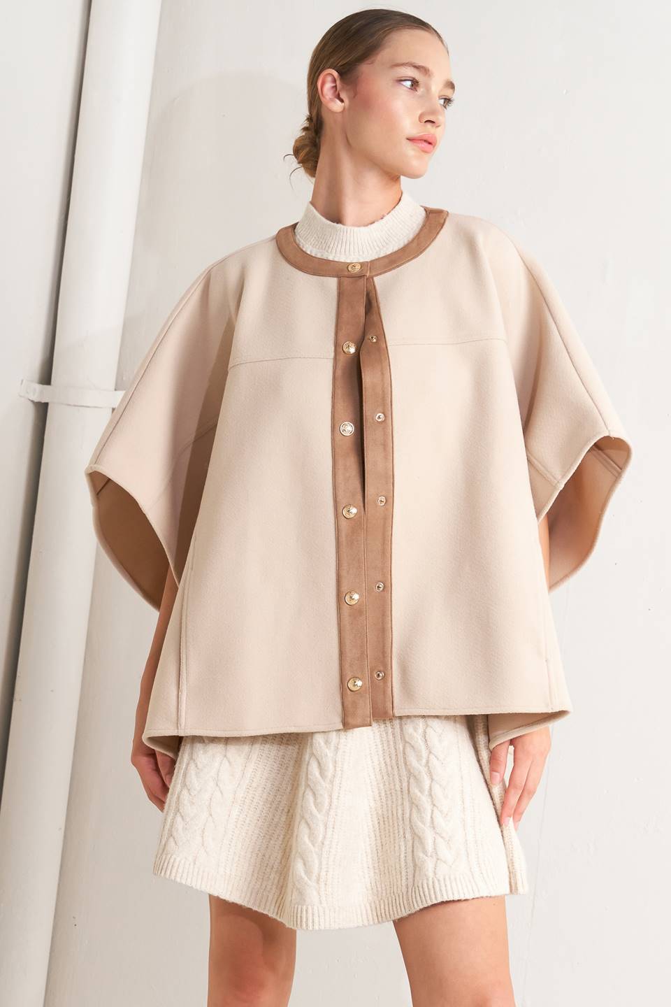 A woven felt capelet featuring round neckline with faux leather binding, front button down and side tab