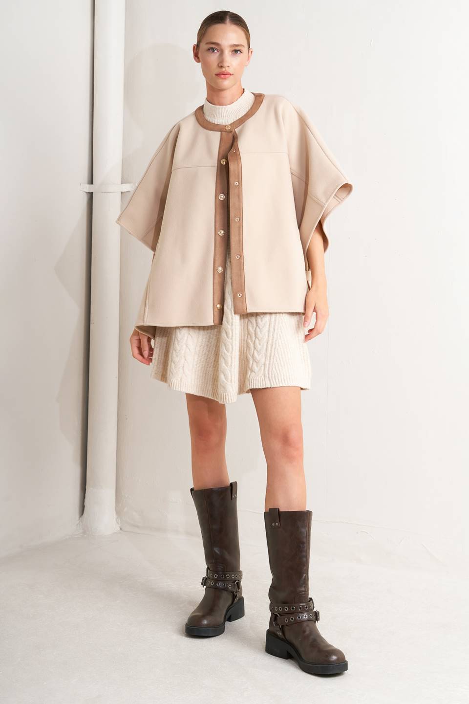 A woven felt capelet featuring round neckline with faux leather binding, front button down and side tab