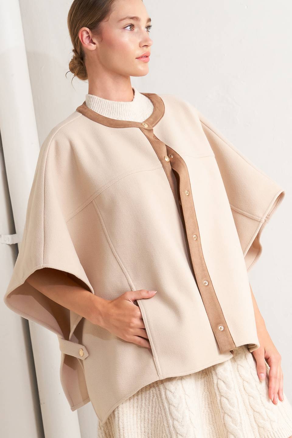 A woven felt capelet featuring round neckline with faux leather binding, front button down and side tab