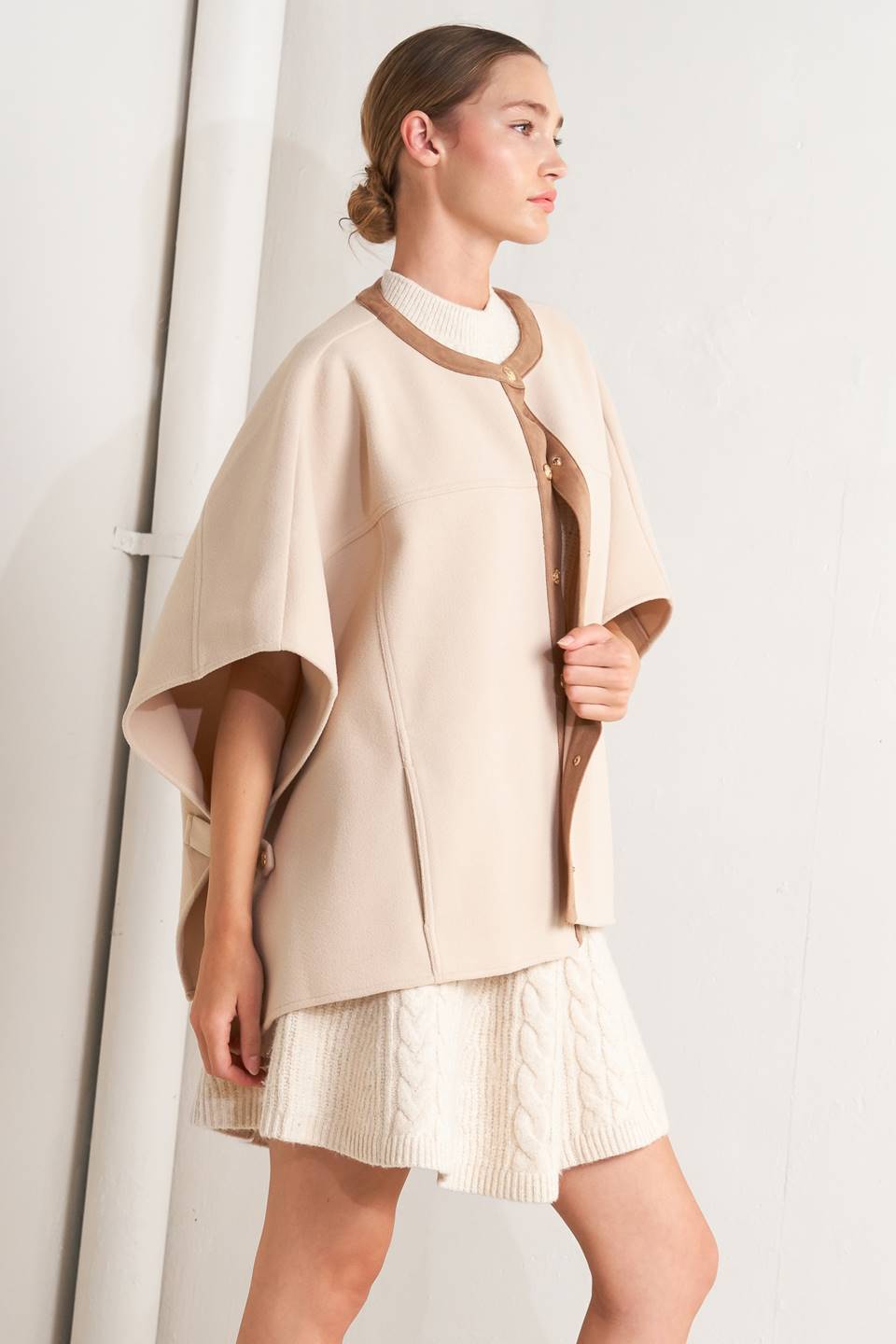 A woven felt capelet featuring round neckline with faux leather binding, front button down and side tab