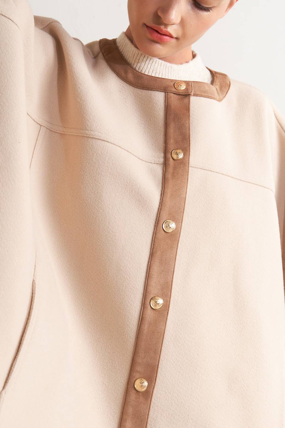 A woven felt capelet featuring round neckline with faux leather binding, front button down and side tab