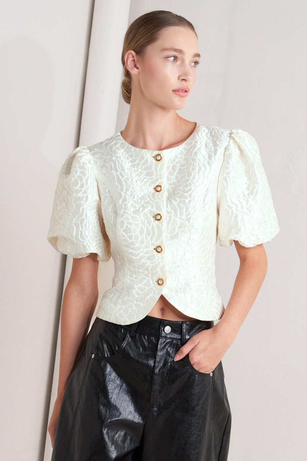 A textured woven top featuring round neckline, short puff sleeve and front button down.