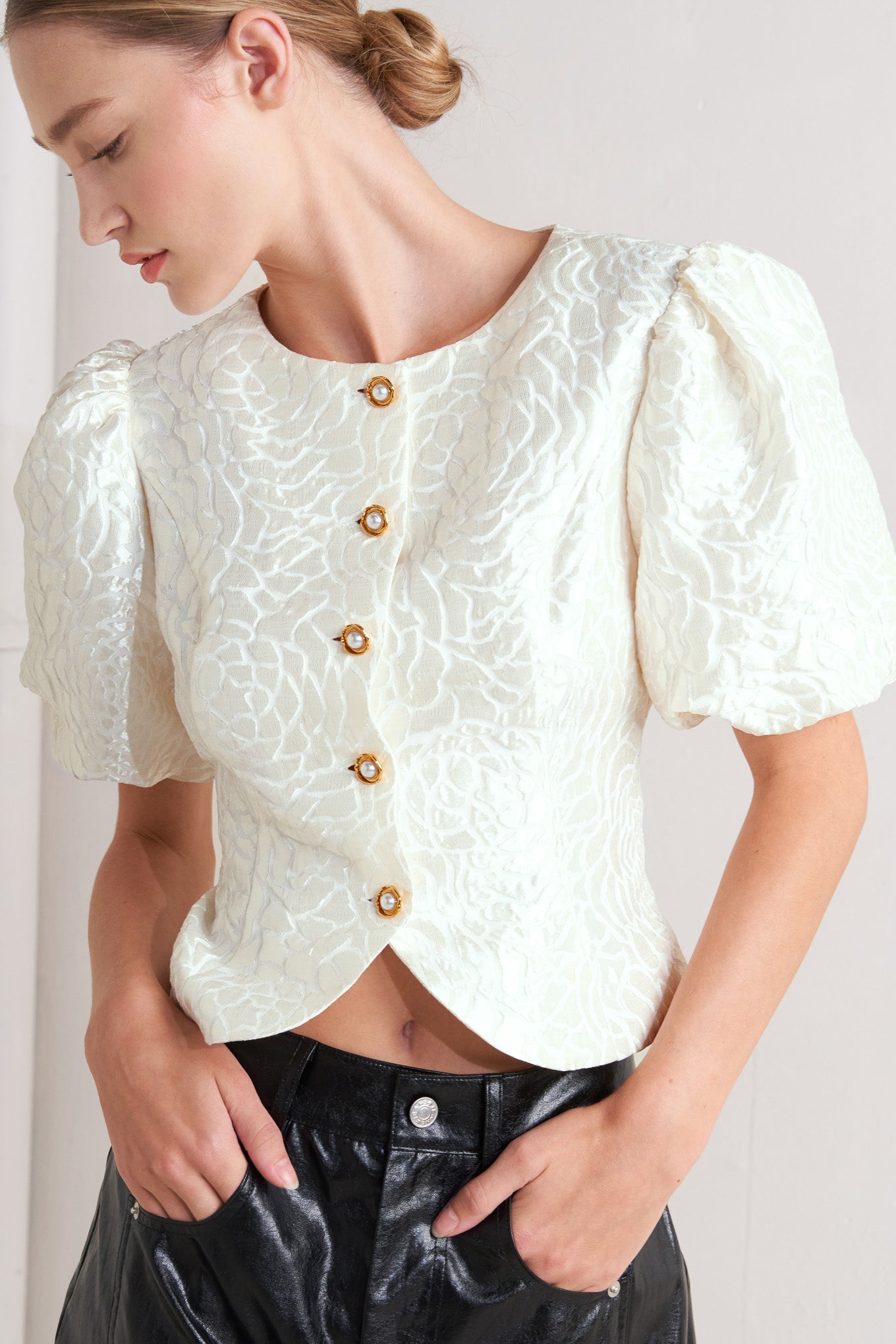 A textured woven top featuring round neckline, short puff sleeve and front button down.
