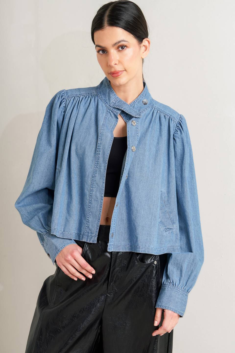 Woman wearing a blue denim jacket over a black top and pants on a plain background - FLYING TOMATO