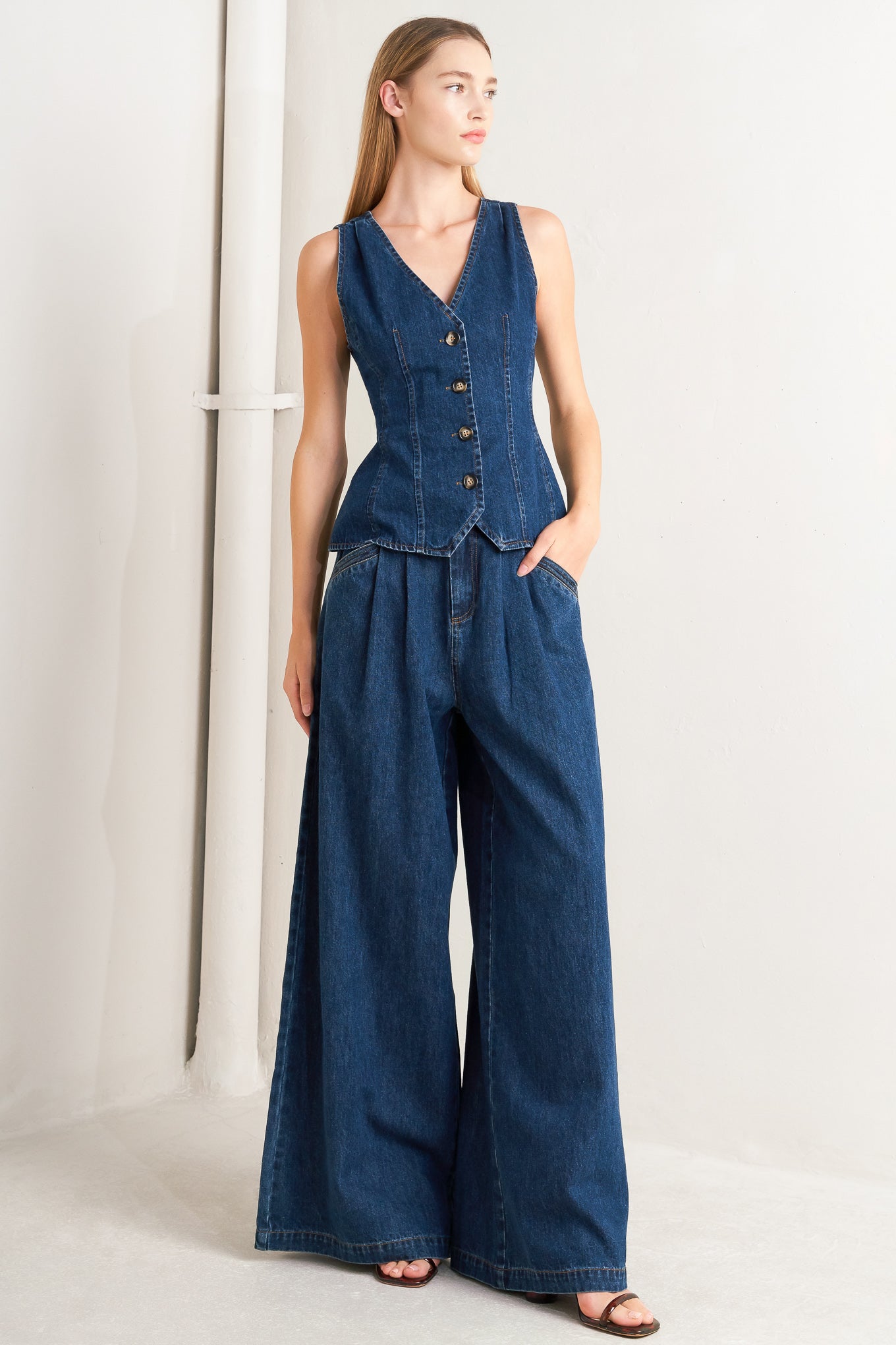 A denim vest featuring front and back V neckline and front button closure.