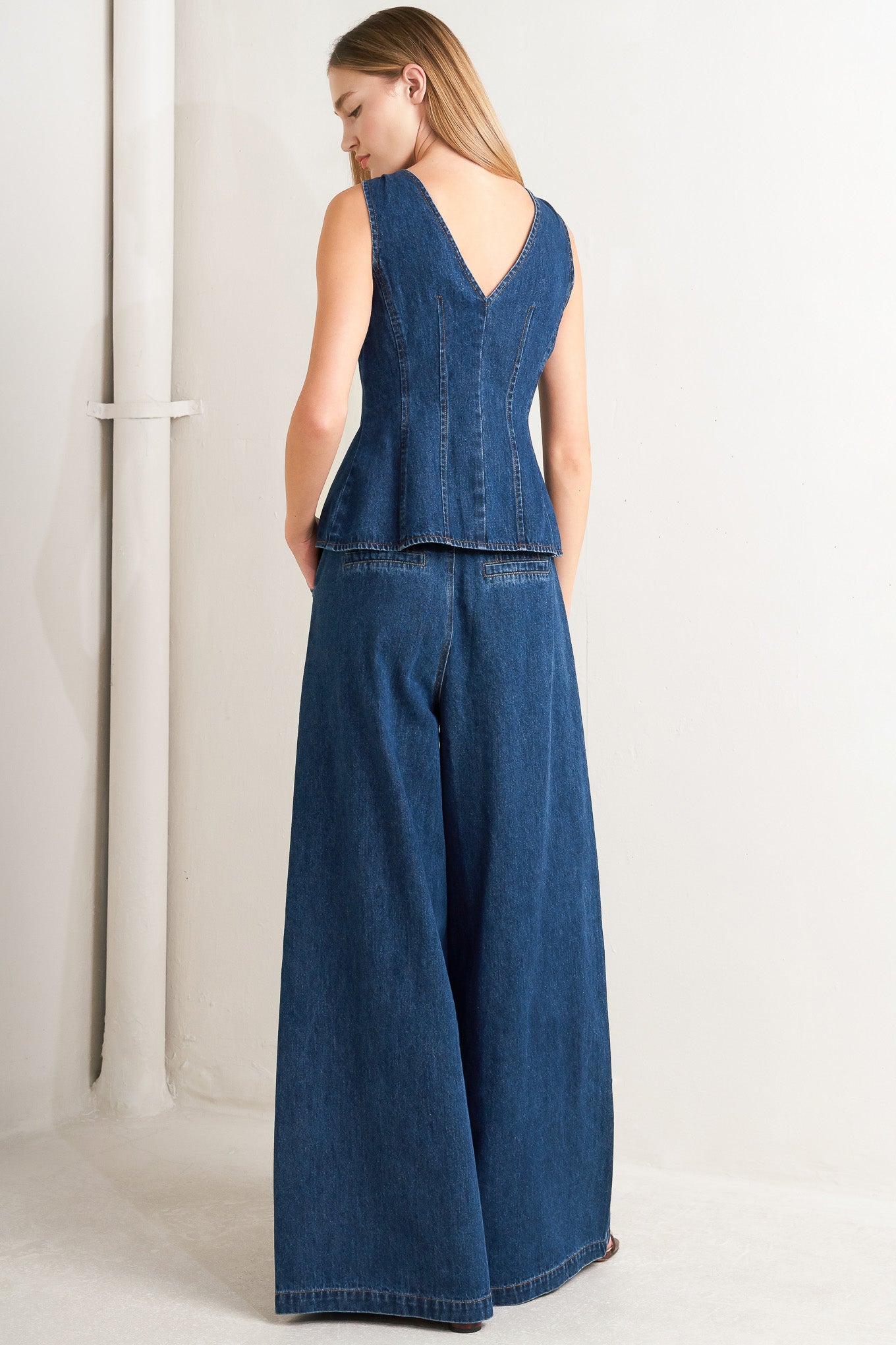 A denim vest featuring front and back V neckline and front button closure.