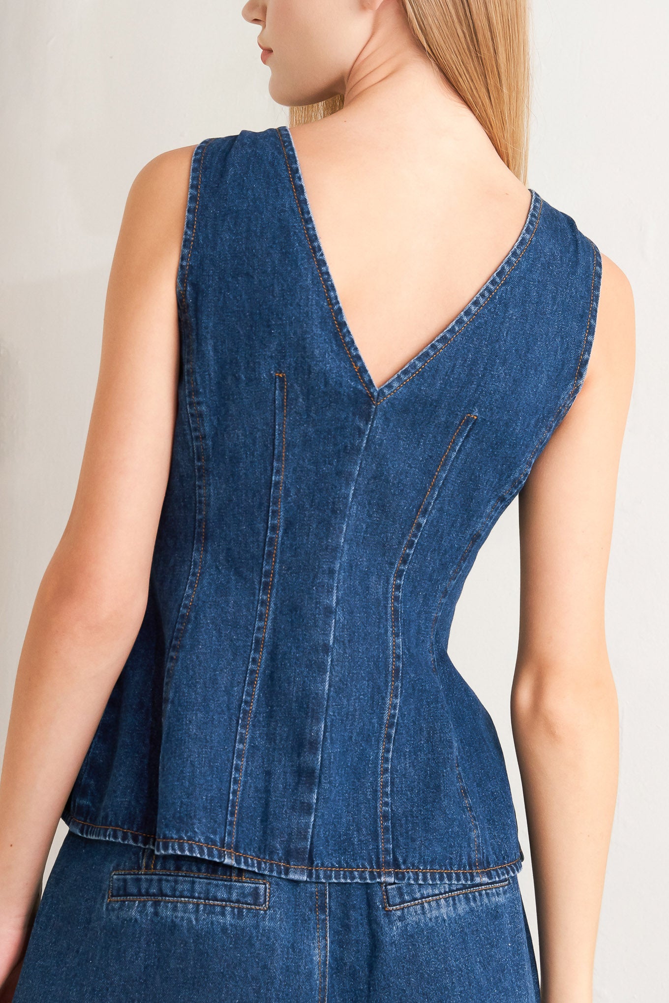 A denim vest featuring front and back V neckline and front button closure.