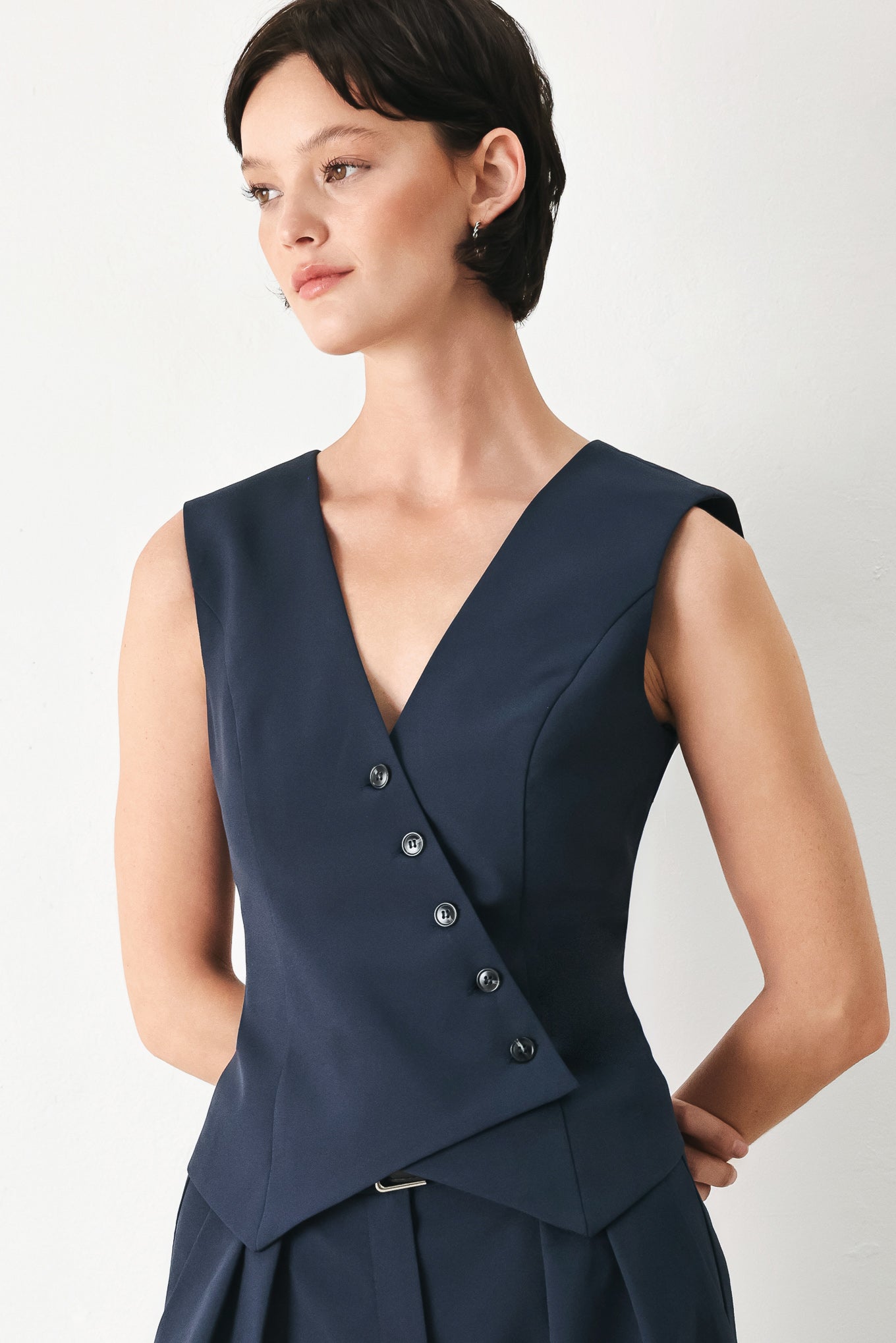 Woman wearing a navy blue sleeveless vest with asymmetrical overlap and buttons | FREEMARKET