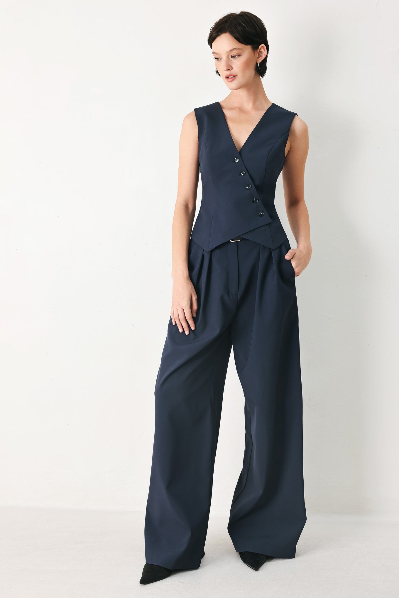 Woman wearing a navy blue sleeveless vest with asymmetrical overlap and buttons | FREEMARKET