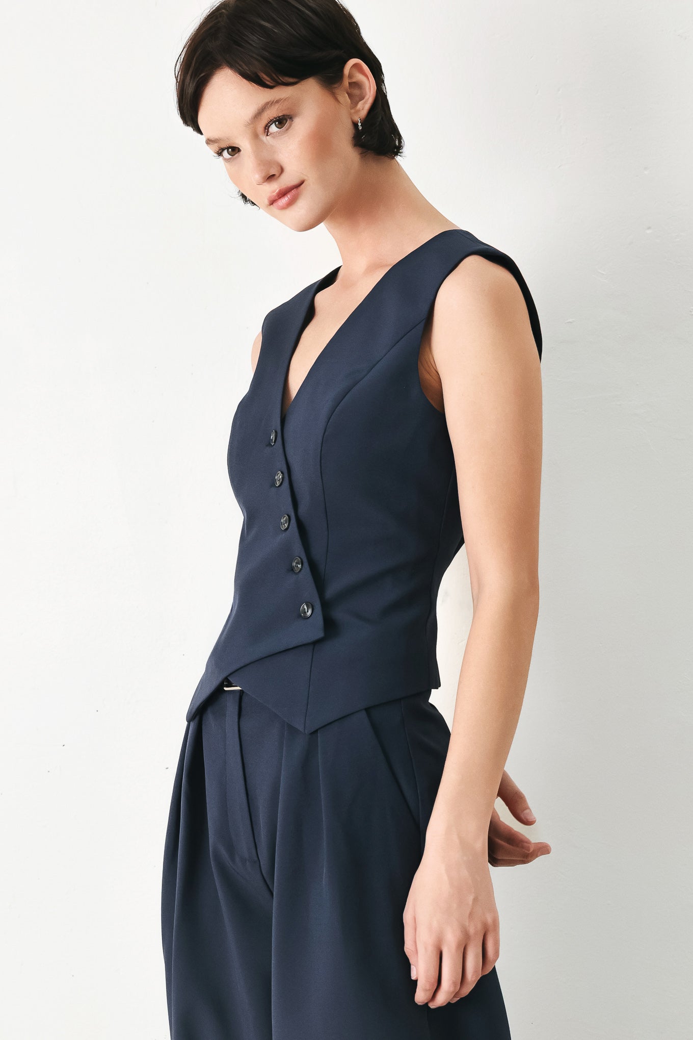 Woman wearing a navy blue sleeveless vest with asymmetrical overlap and buttons | FREEMARKET