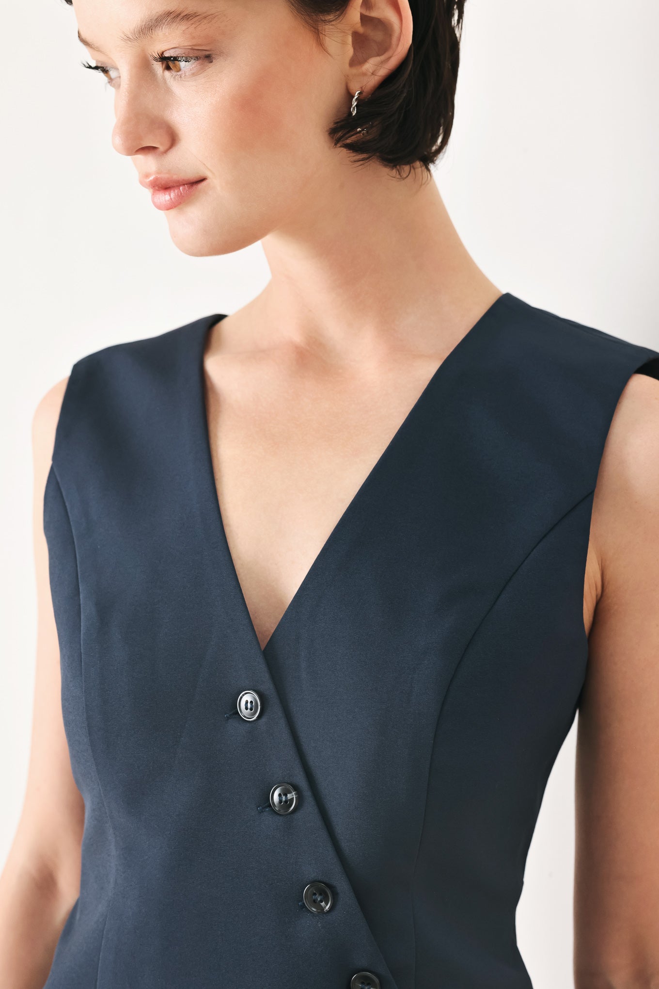 Woman wearing a navy blue sleeveless vest with asymmetrical overlap and buttons | FREEMARKET