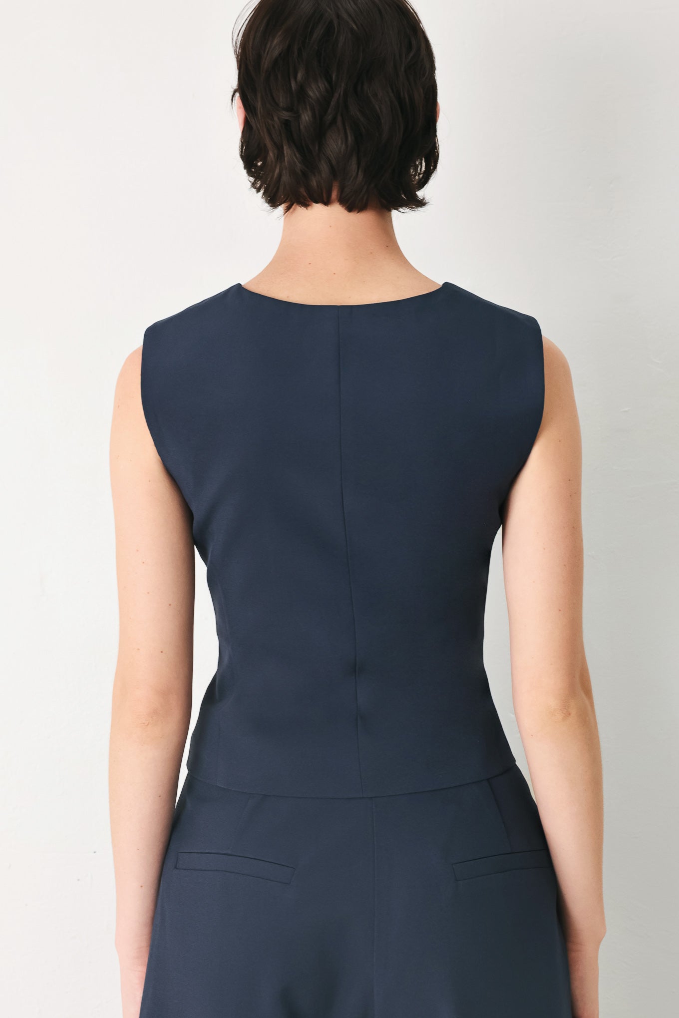 Woman wearing a navy blue sleeveless vest with asymmetrical overlap and buttons | FREEMARKET