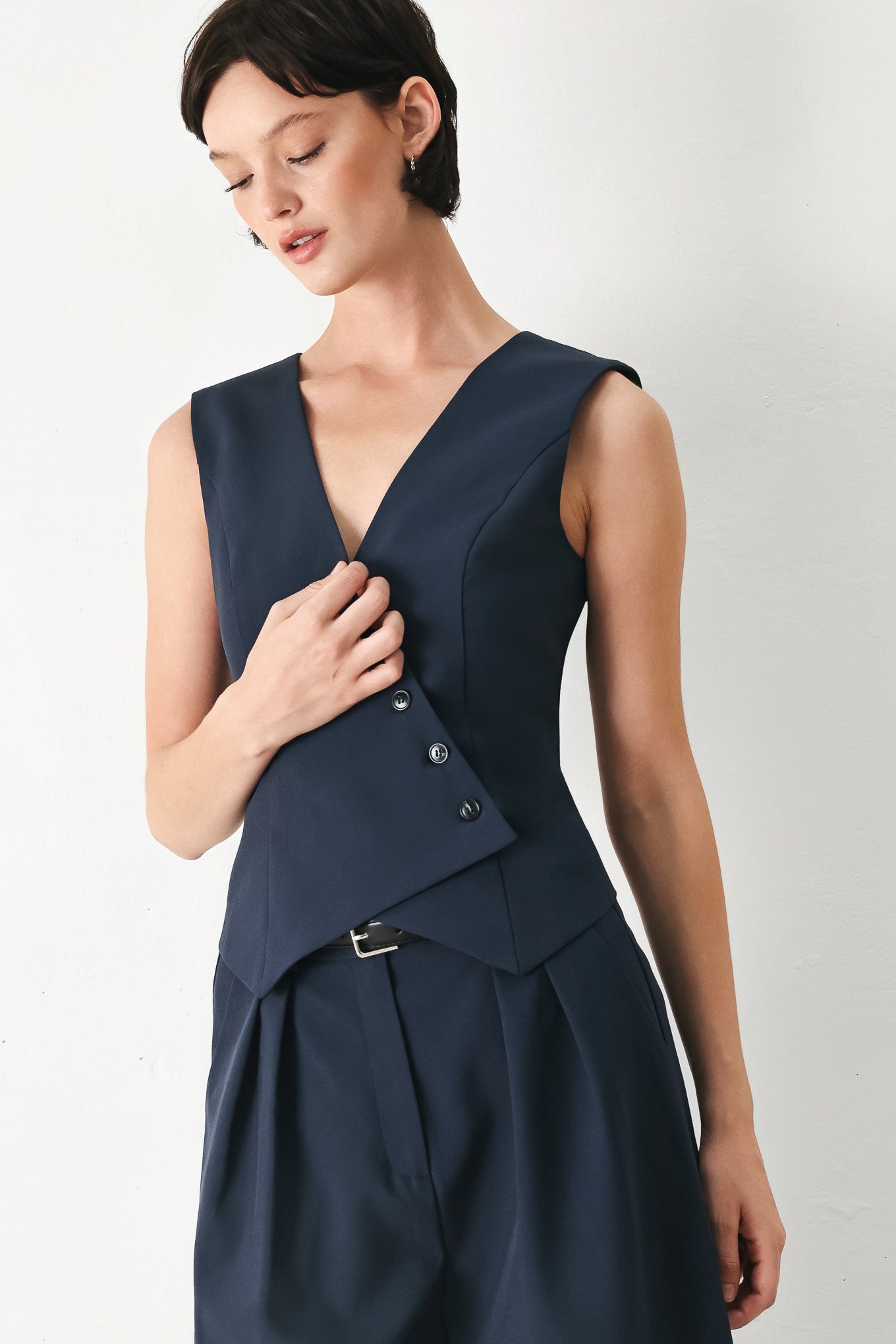 Woman wearing a navy blue sleeveless vest with asymmetrical overlap and buttons | FREEMARKET