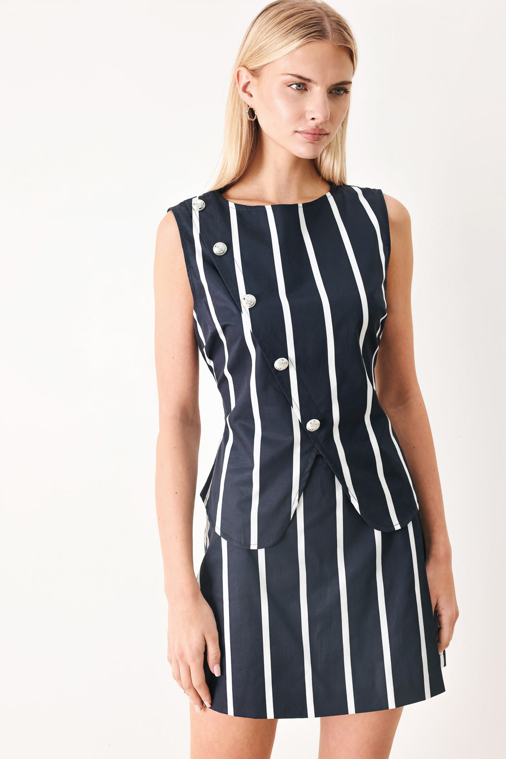 Woman wearing a navy blue top with white stripes and silver buttons featuring round neckline, sleeveless, diagonal button detail and back zipper closure | FREEMARKET