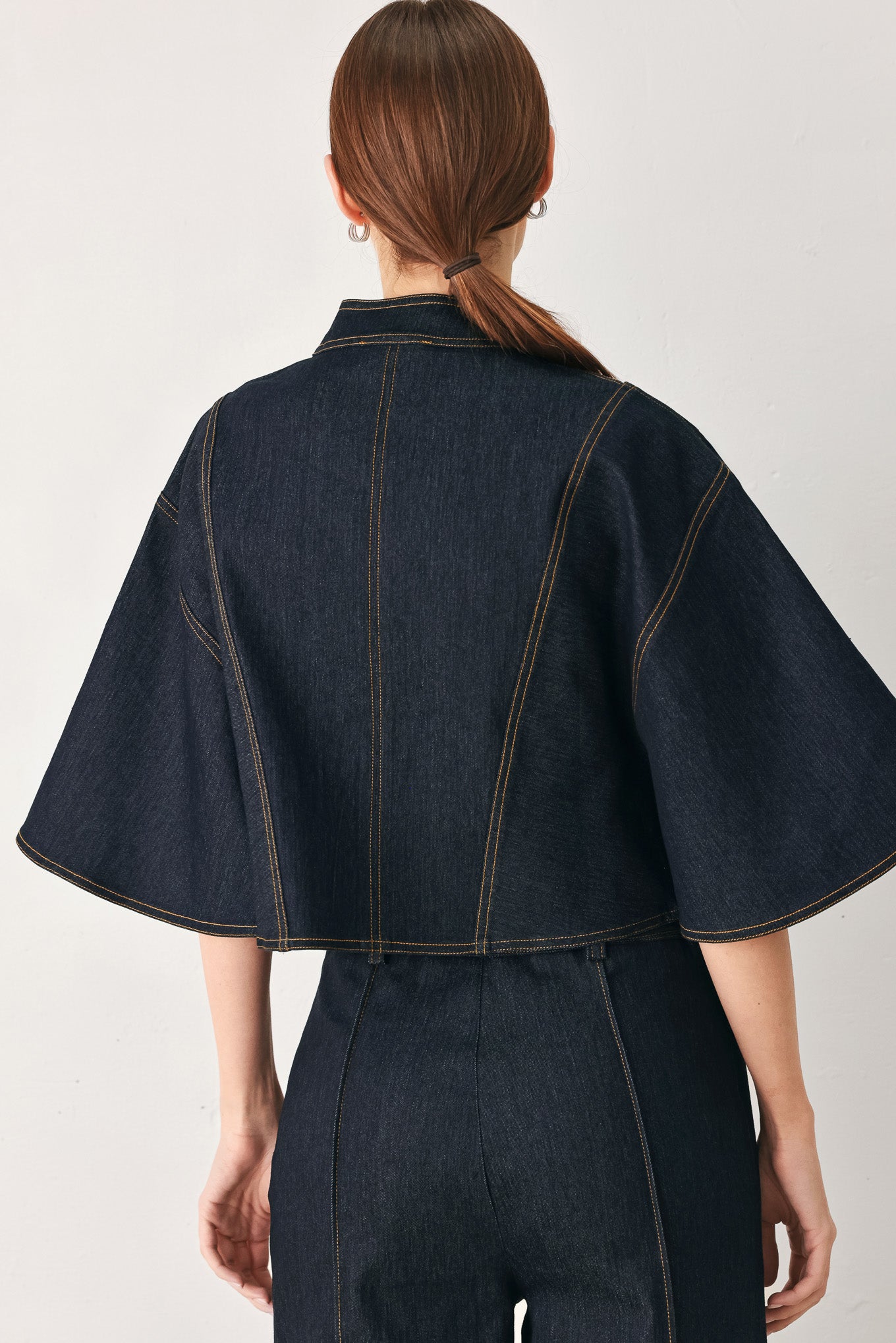Woman wearing a dark denim capelet top with front zipper closure | FREEMARKET