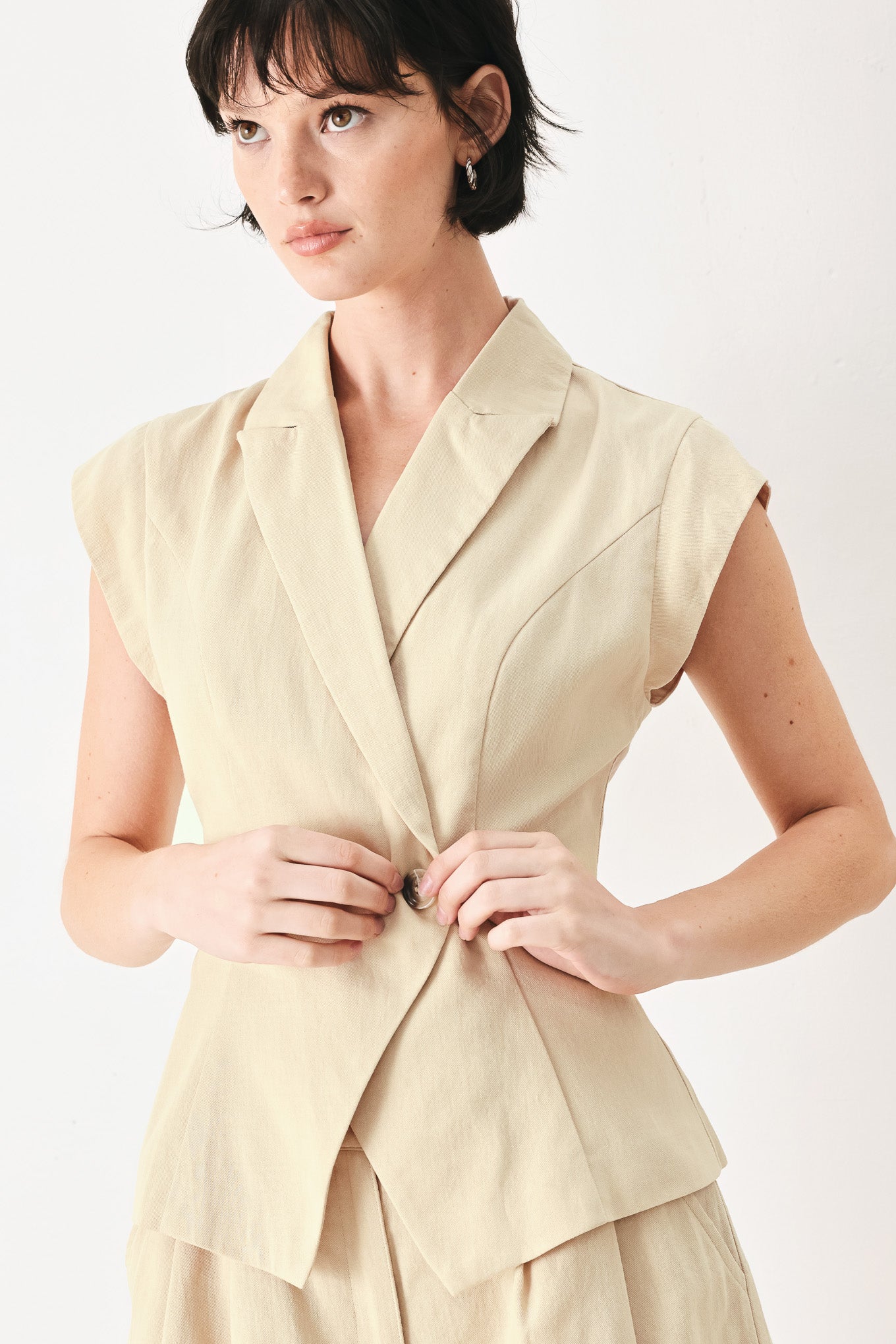 Woman wearing light tan woven vest with collar, cap sleeve and button closure | FREEMARKET