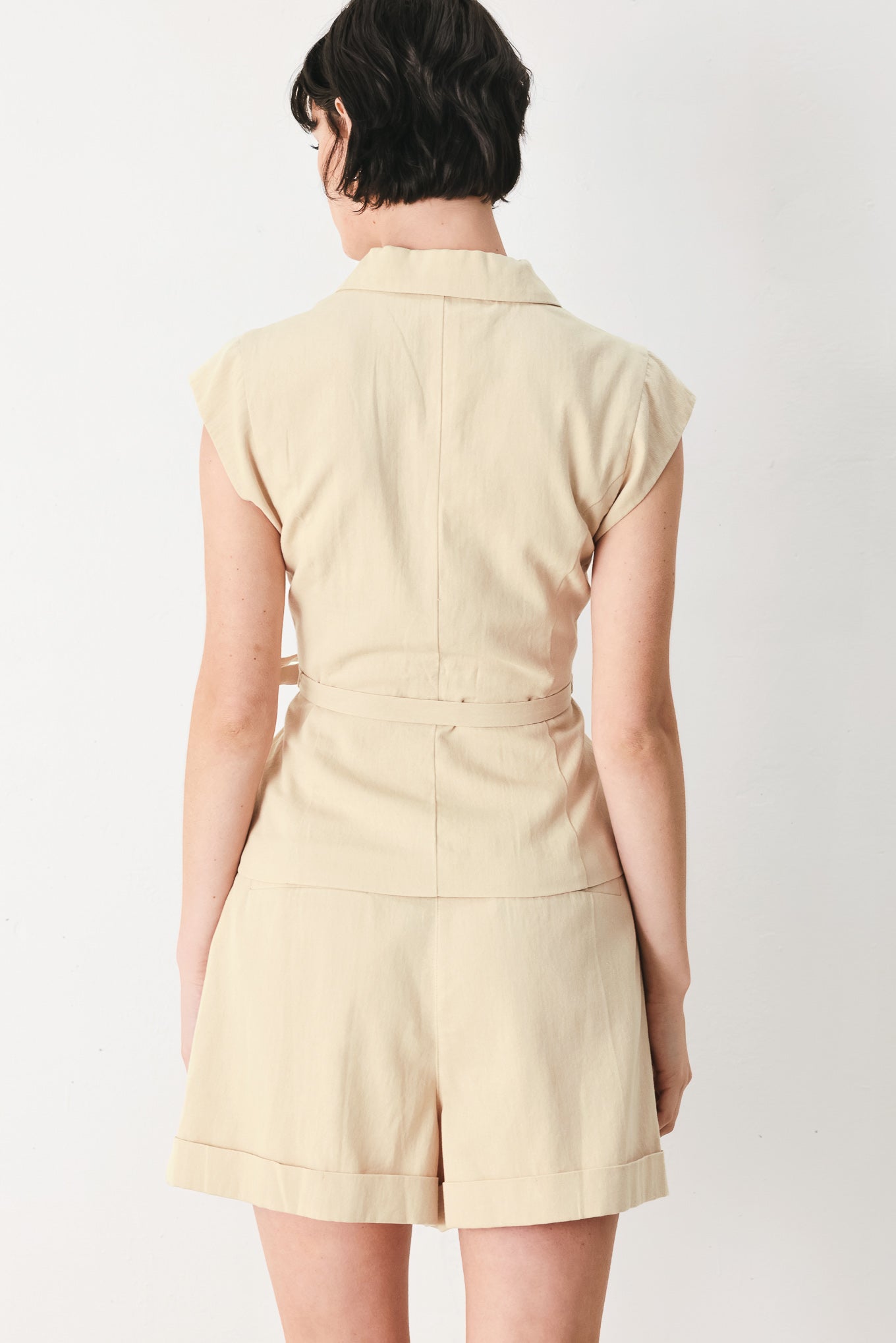 Woman wearing light tan woven vest with collar, cap sleeve and button closure | FREEMARKET