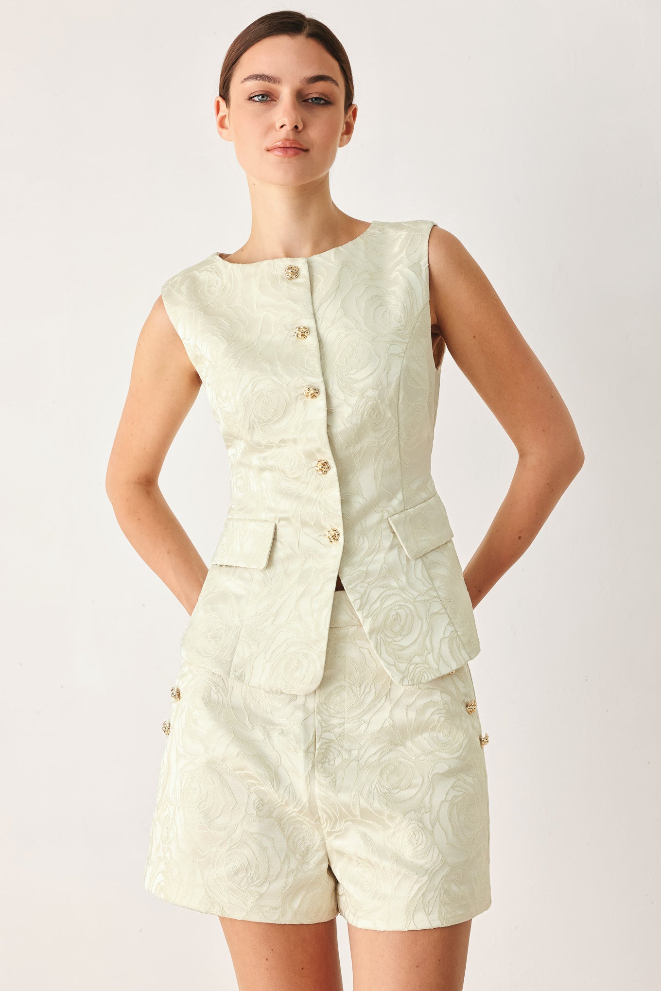 Woman wearing a sleeveless, button-front vest in a light cream or off-white jacquard fabric with small gold-tone buttons | FREEMARKET