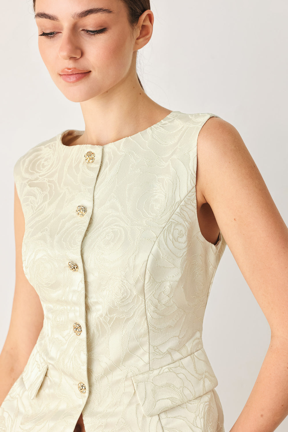 Woman wearing a sleeveless, button-front vest in a light cream or off-white jacquard fabric with small gold-tone buttons | FREEMARKET