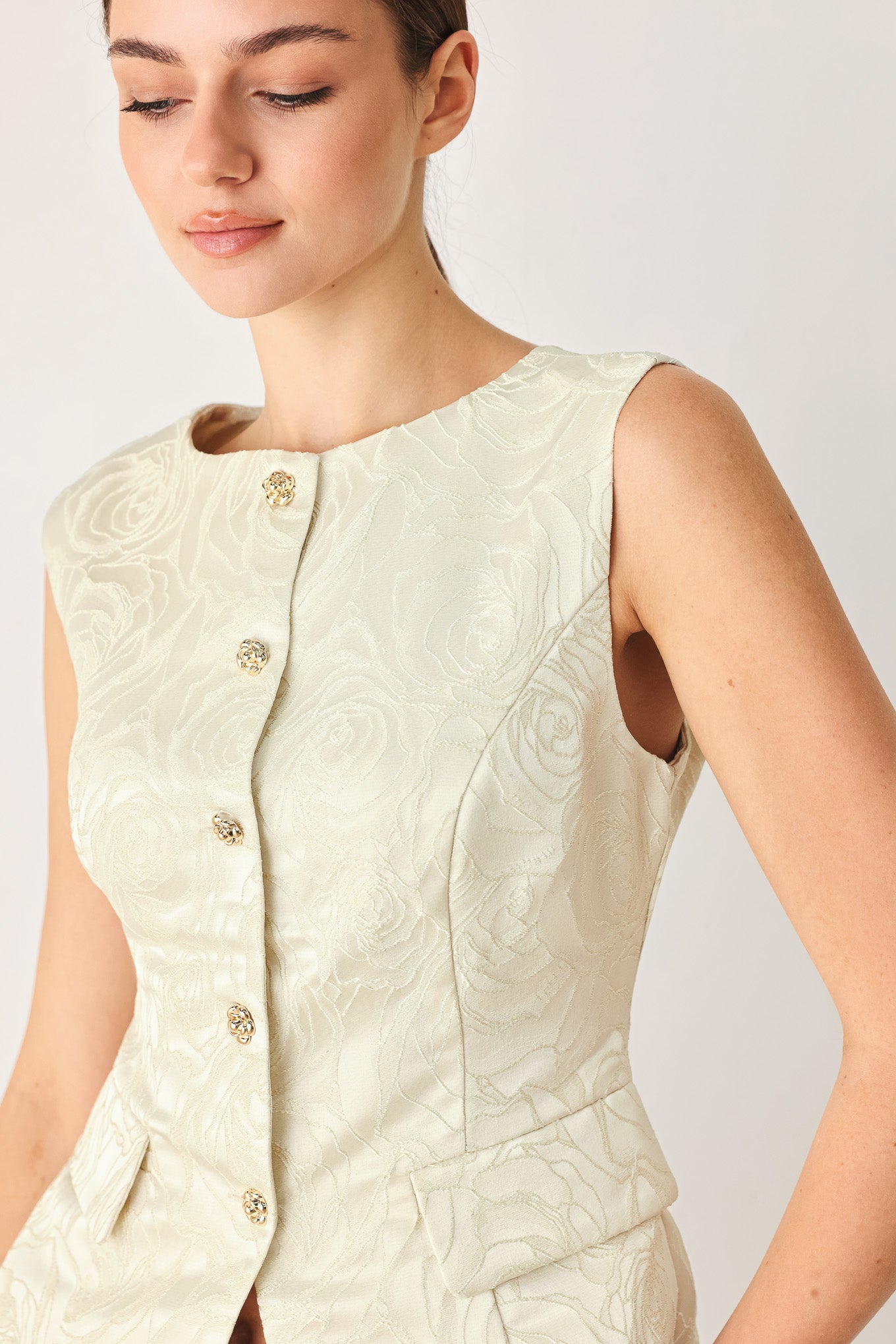 Woman wearing a sleeveless, button-front vest in a light cream or off-white jacquard fabric with small gold-tone buttons | FREEMARKET