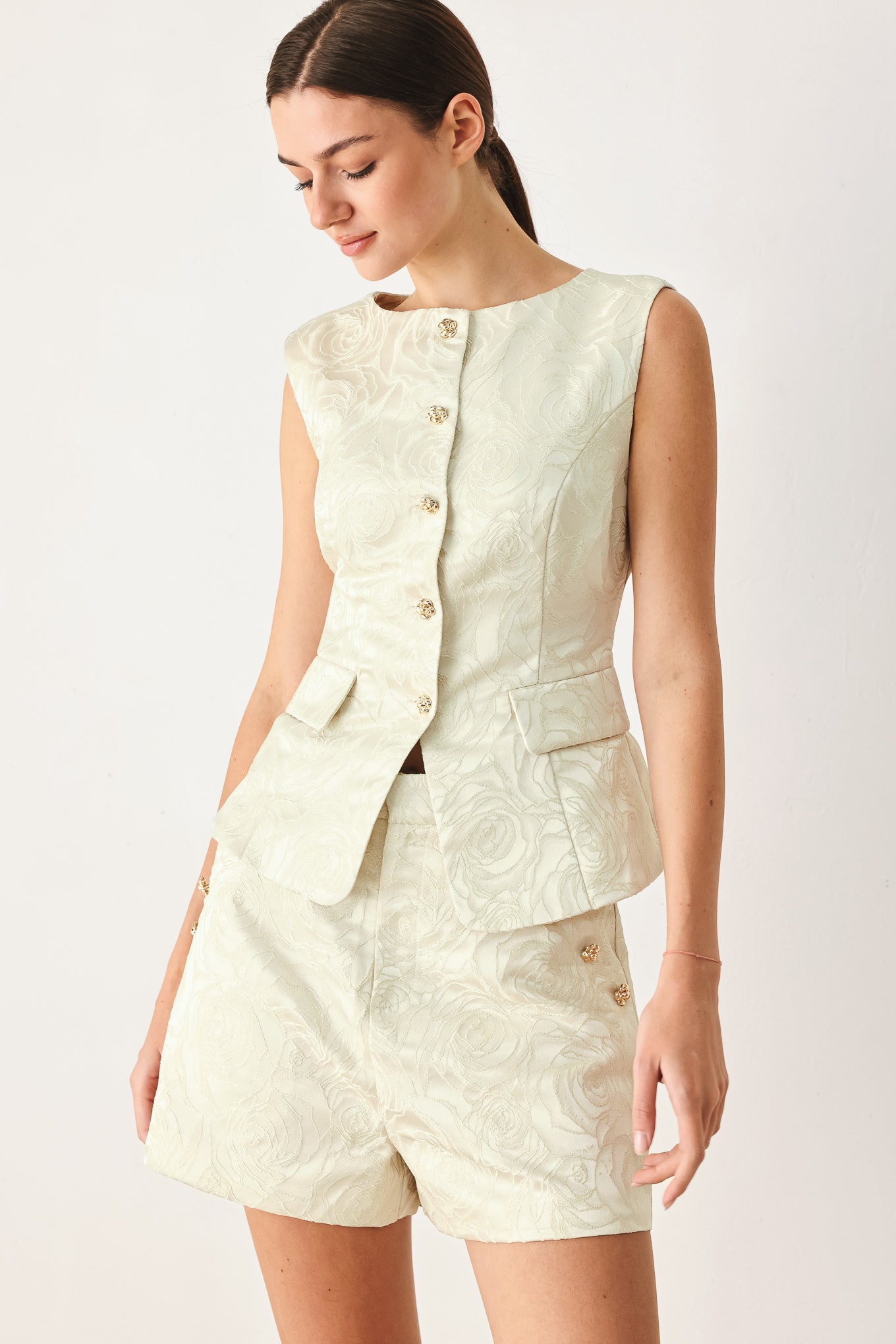 Woman wearing a sleeveless, button-front vest in a light cream or off-white jacquard fabric with small gold-tone buttons | FREEMARKET