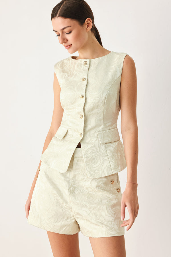 Woman wearing a sleeveless, button-front vest in a light cream or off-white jacquard fabric with small gold-tone buttons | FREEMARKET