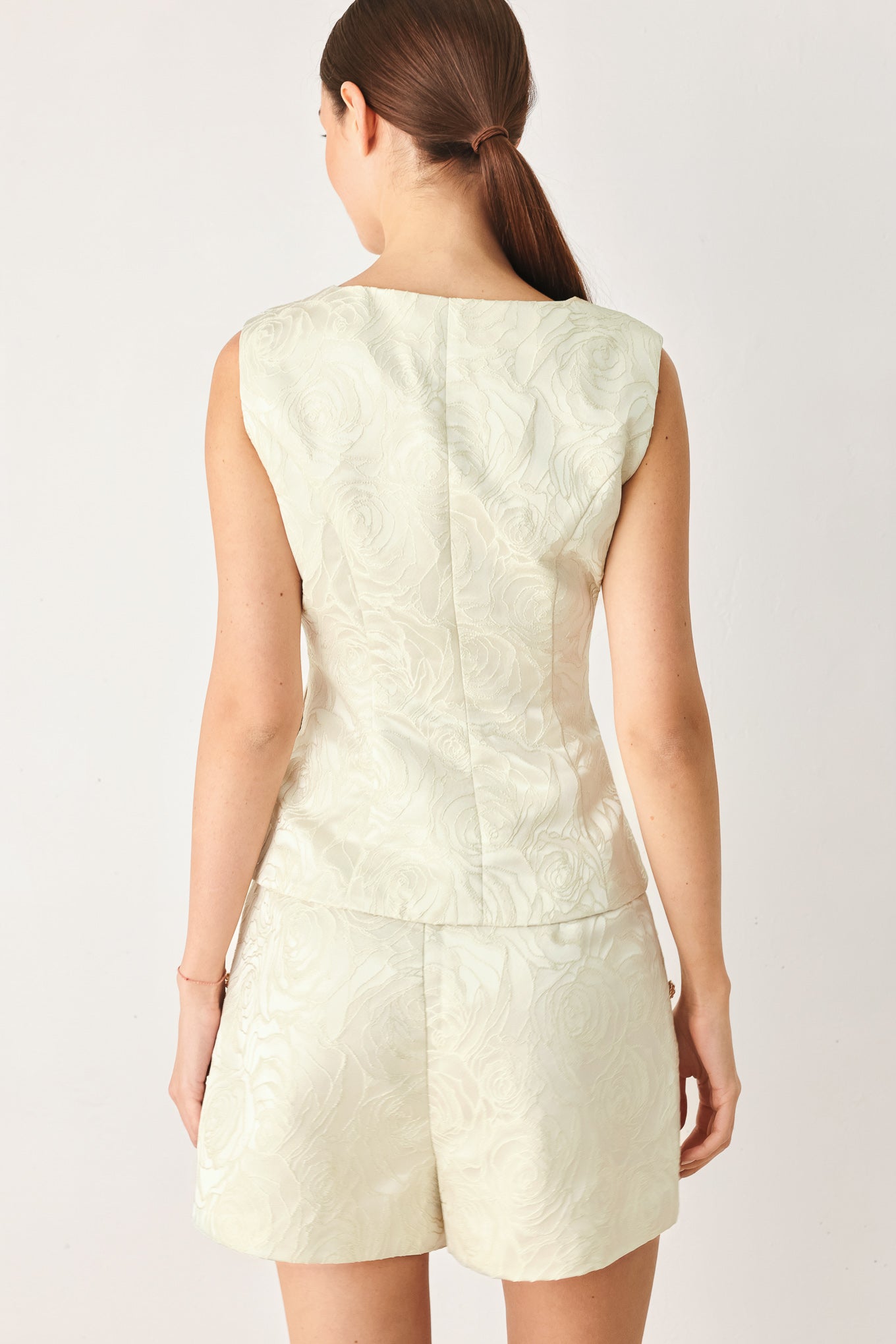 Woman wearing a sleeveless, button-front vest in a light cream or off-white jacquard fabric with small gold-tone buttons | FREEMARKET