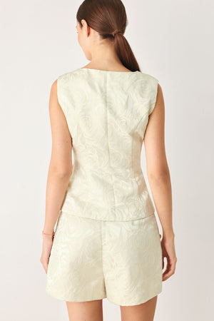 Woman wearing a sleeveless, button-front vest in a light cream or off-white jacquard fabric with small gold-tone buttons | FREEMARKET