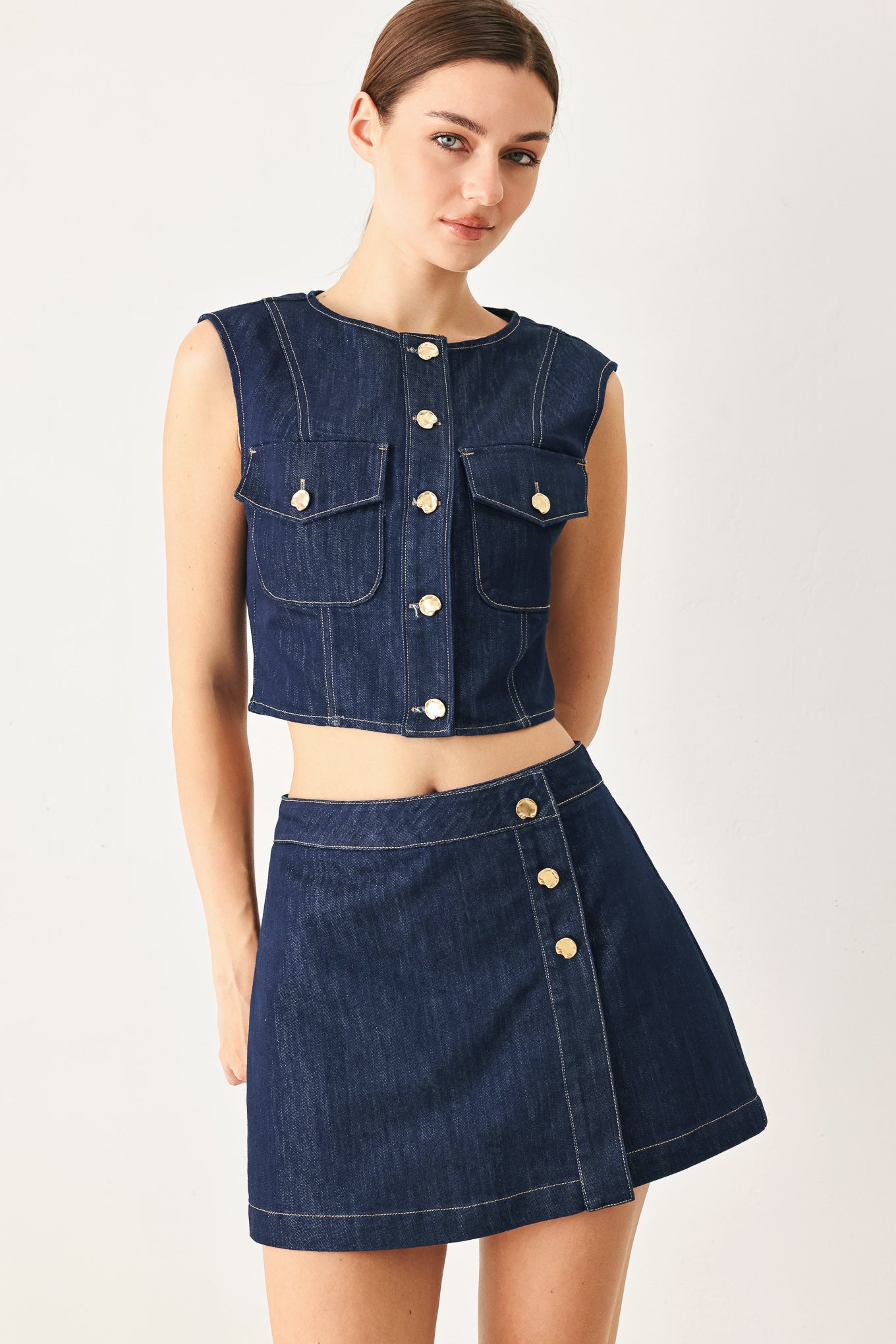 Woman wearing a denim outfit with a vest and skirt on a white background