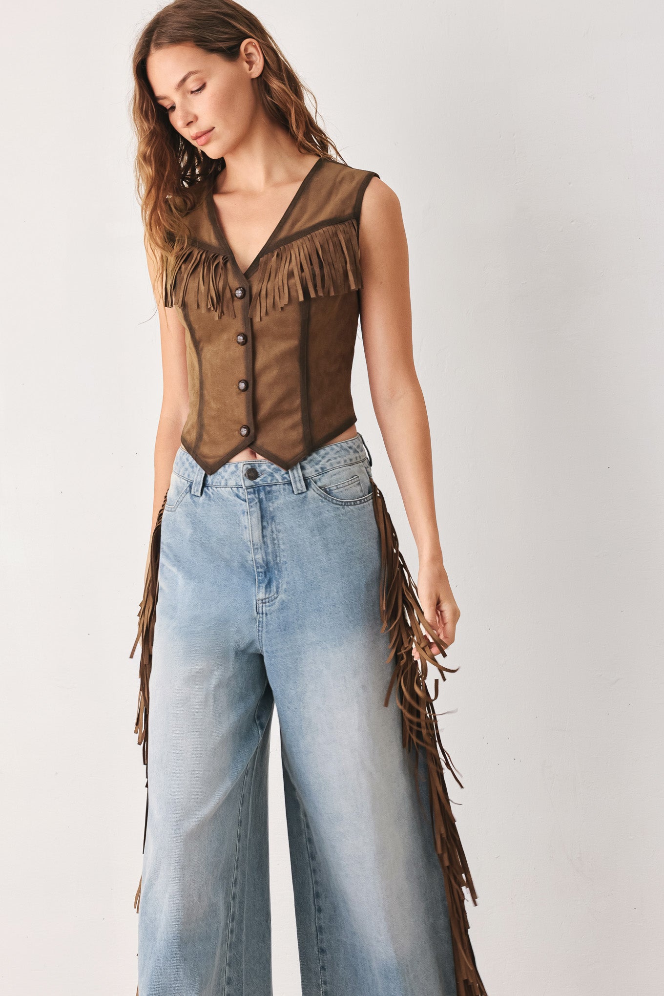 A woman modeling a brown faux-suede vest with fringe trim and button-front detailing | FREEMARKET