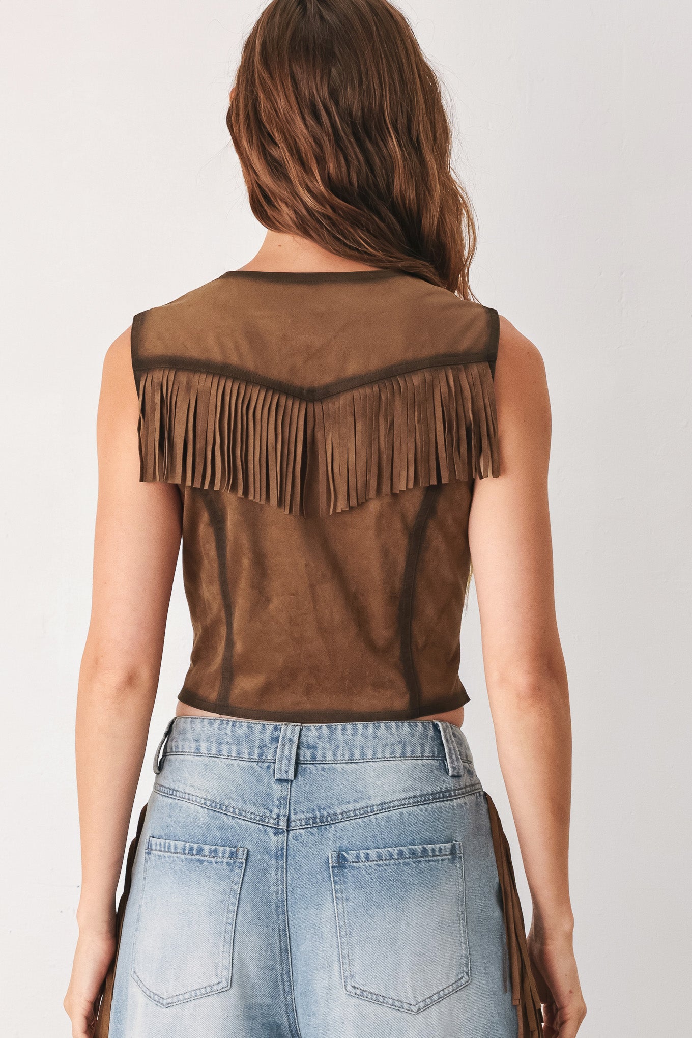 A woman modeling a brown faux-suede vest with fringe trim and button-front detailing | FREEMARKET