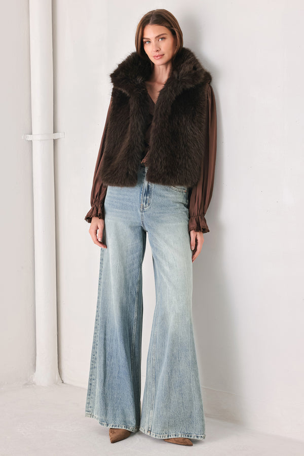 A model wearing a brown faux fur vest over a brown long-sleeve top, paired with wide-leg light blue jeans | FREEMARKET