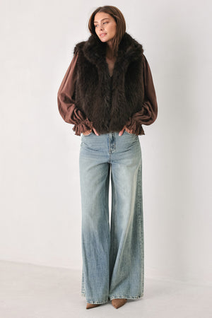 A model wearing a brown faux fur vest over a brown long-sleeve top, paired with wide-leg light blue jeans | FREEMARKET