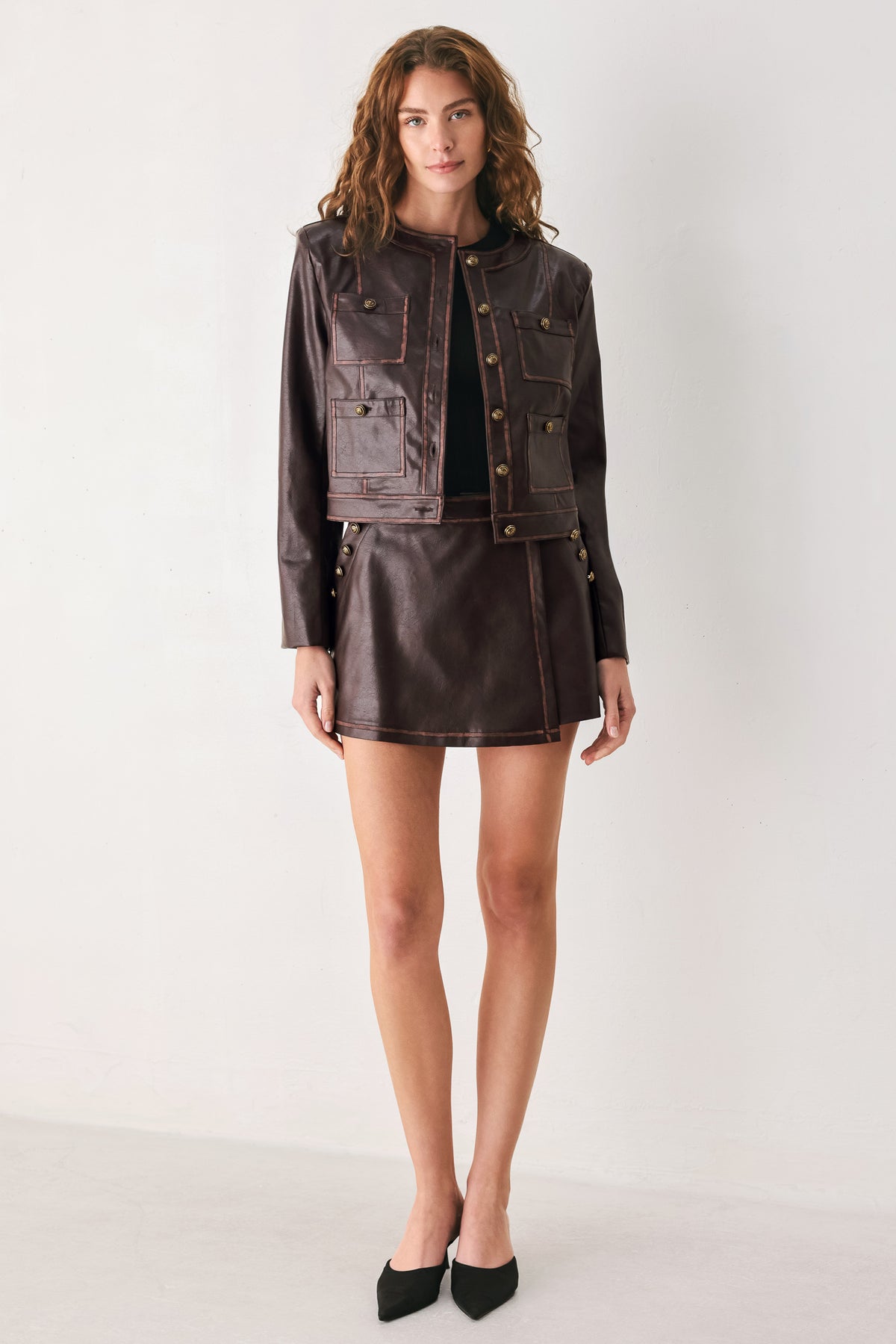 Woman wearing a brown long sleeve faux leather cropped jacket with button closure and small chest pockets with button adornments | FREEMARKET