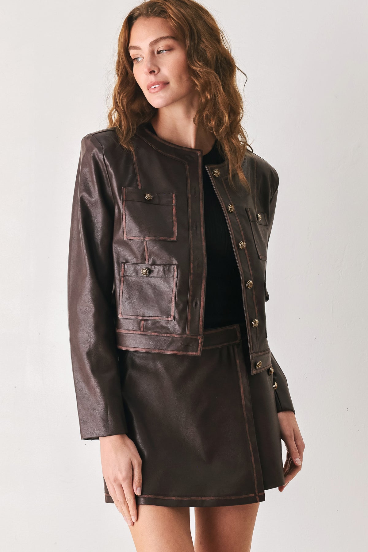 Woman wearing a brown long sleeve faux leather cropped jacket with button closure and small chest pockets with button adornments | FREEMARKET