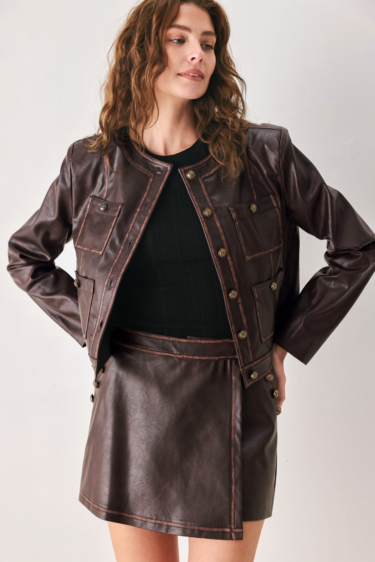 Woman wearing a brown long sleeve faux leather cropped jacket with button closure and small chest pockets with button adornments | FREEMARKET