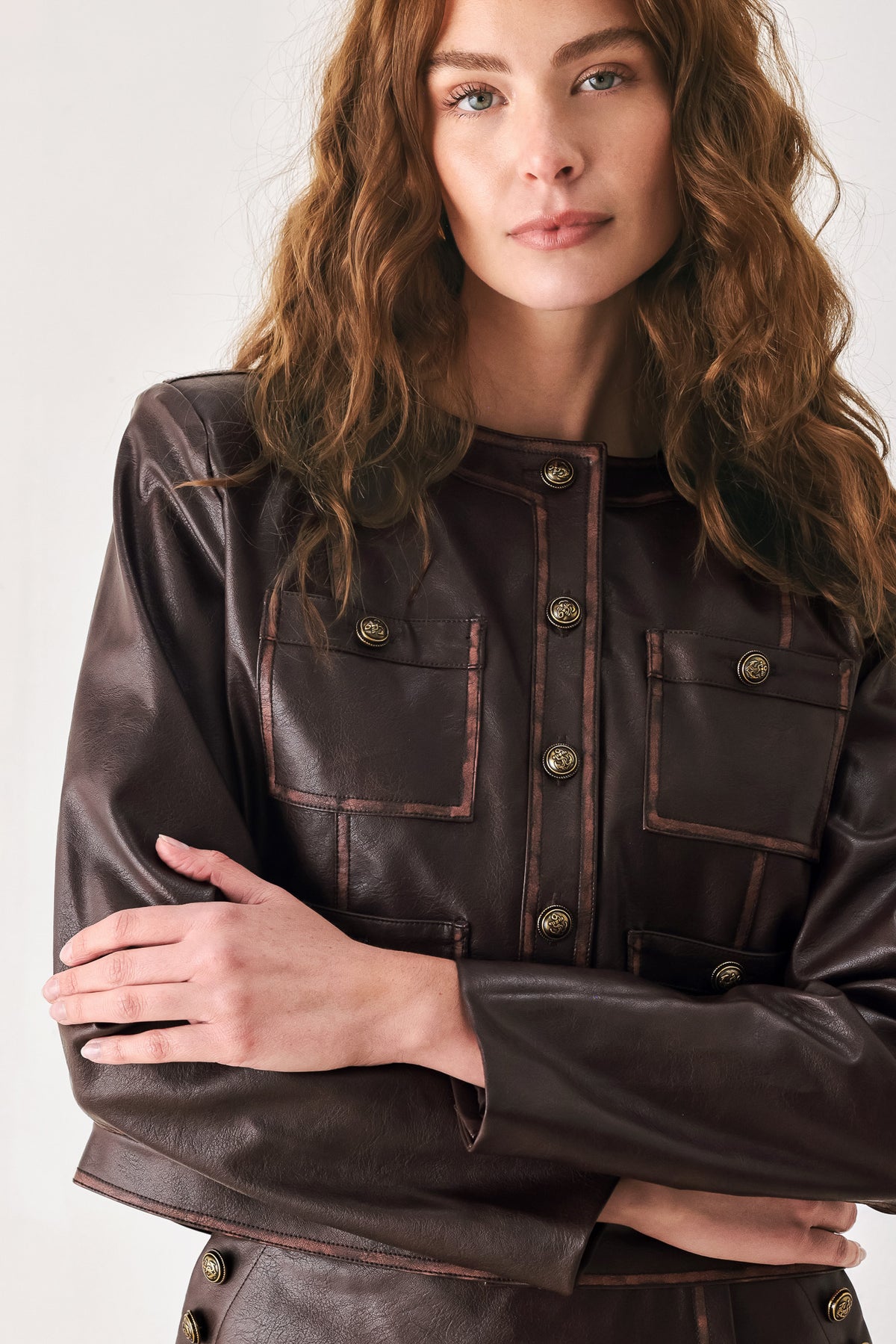 Woman wearing a brown long sleeve faux leather cropped jacket with button closure and small chest pockets with button adornments | FREEMARKET