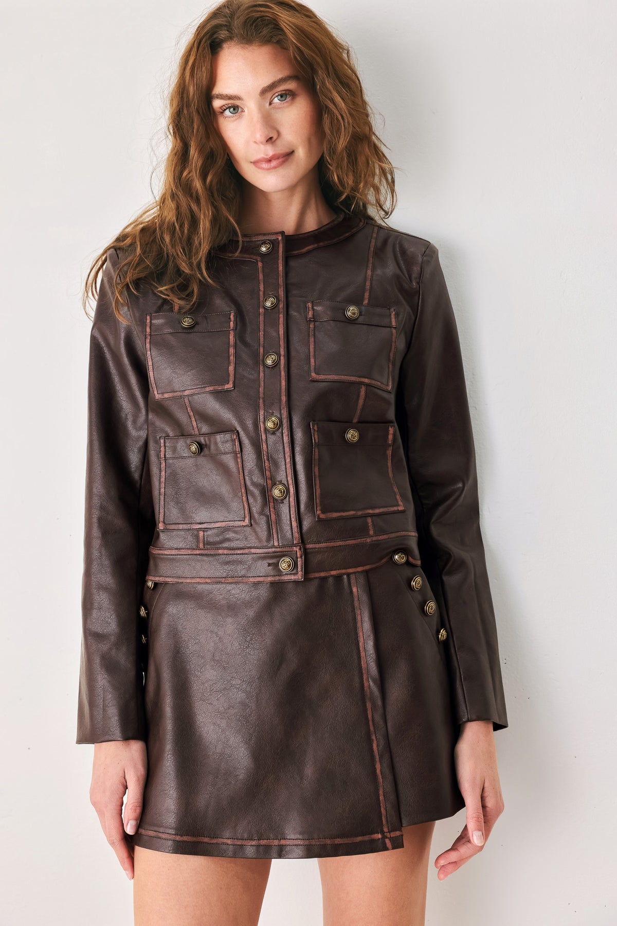 Woman wearing a brown long sleeve faux leather cropped jacket with button closure and small chest pockets with button adornments | FREEMARKET