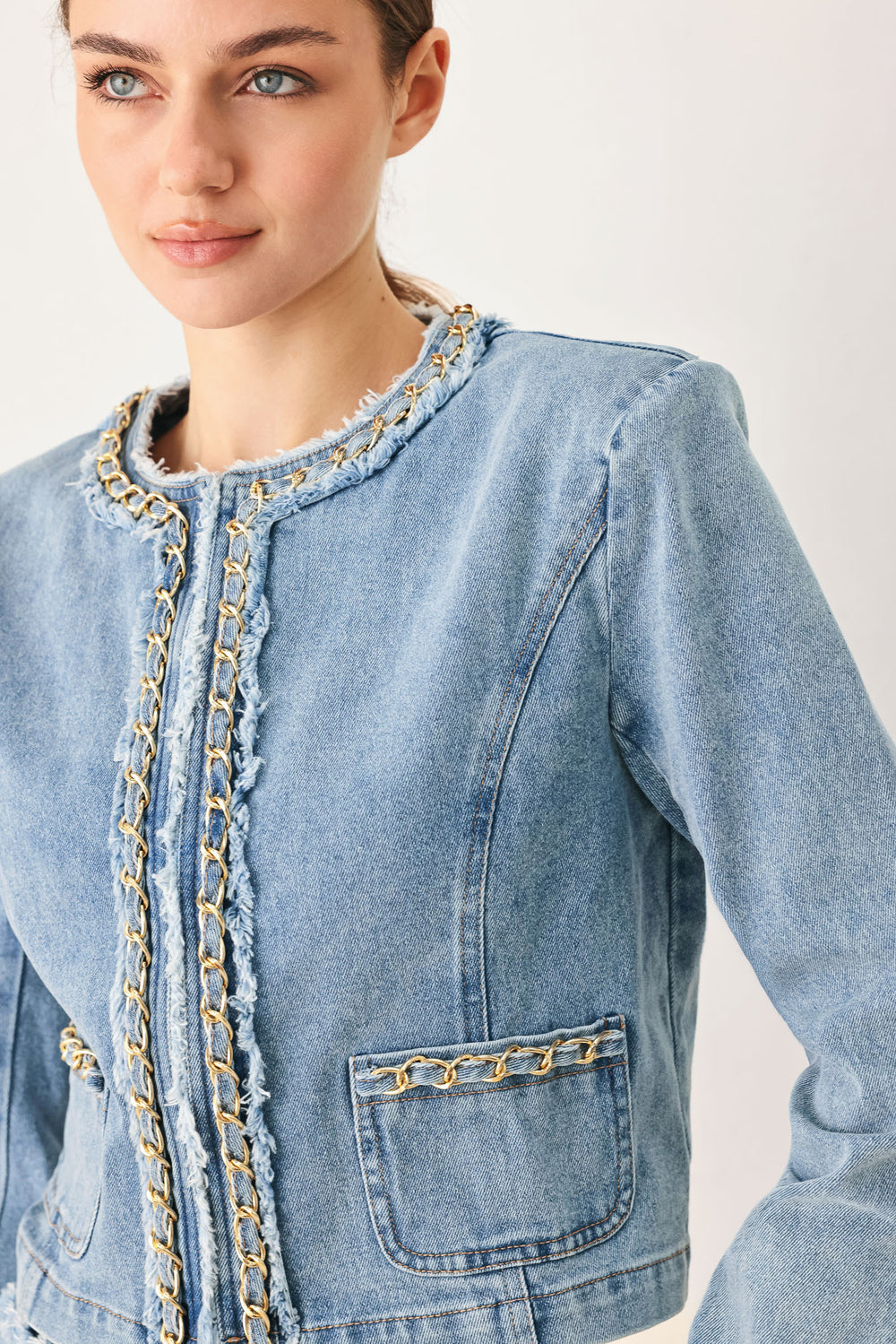 Woman wearing a light blue denim jacket featuring decorative gold chain trim and frayed details | FREEMARKET