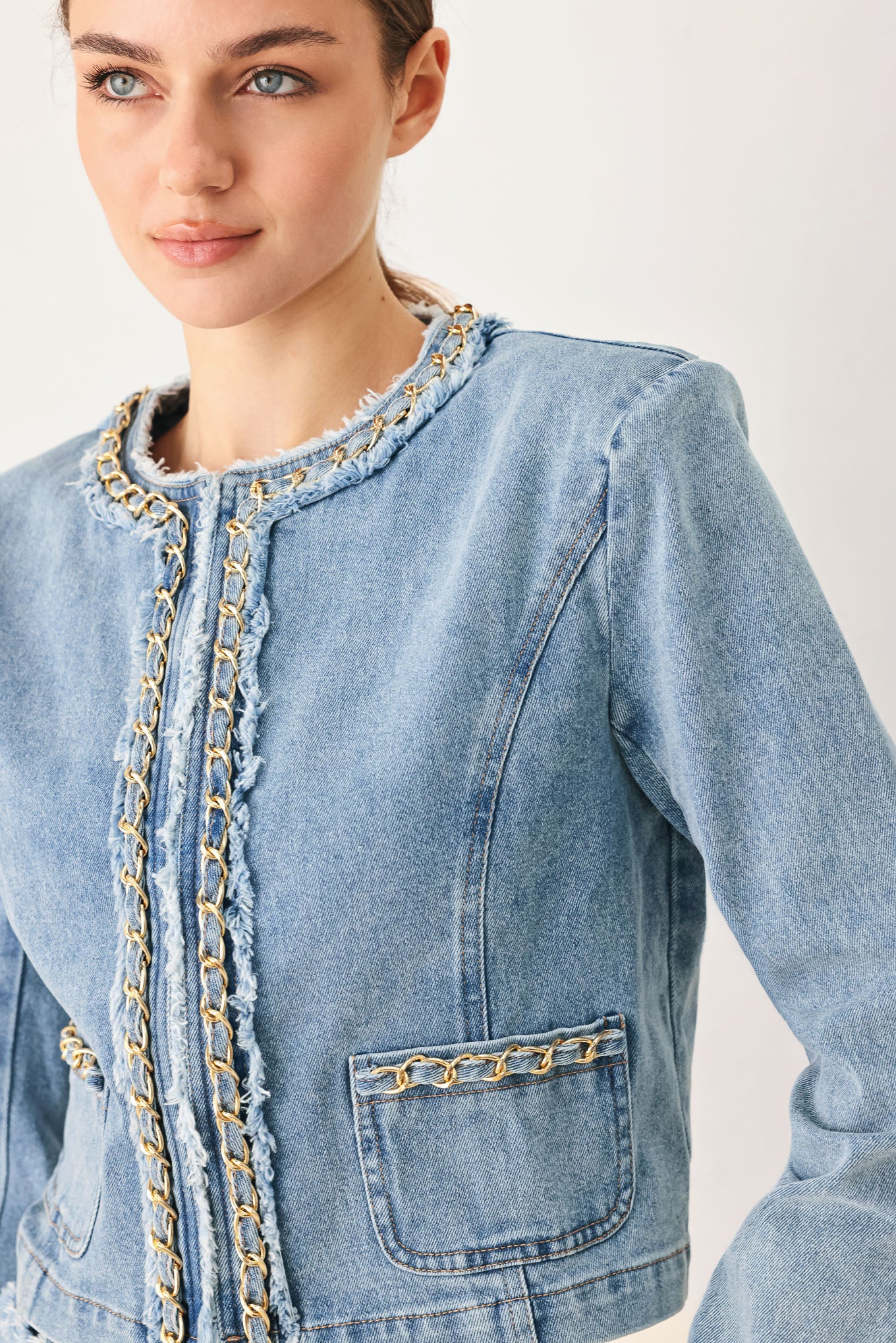 Woman wearing a light blue denim jacket featuring decorative gold chain trim and frayed details | FREEMARKET