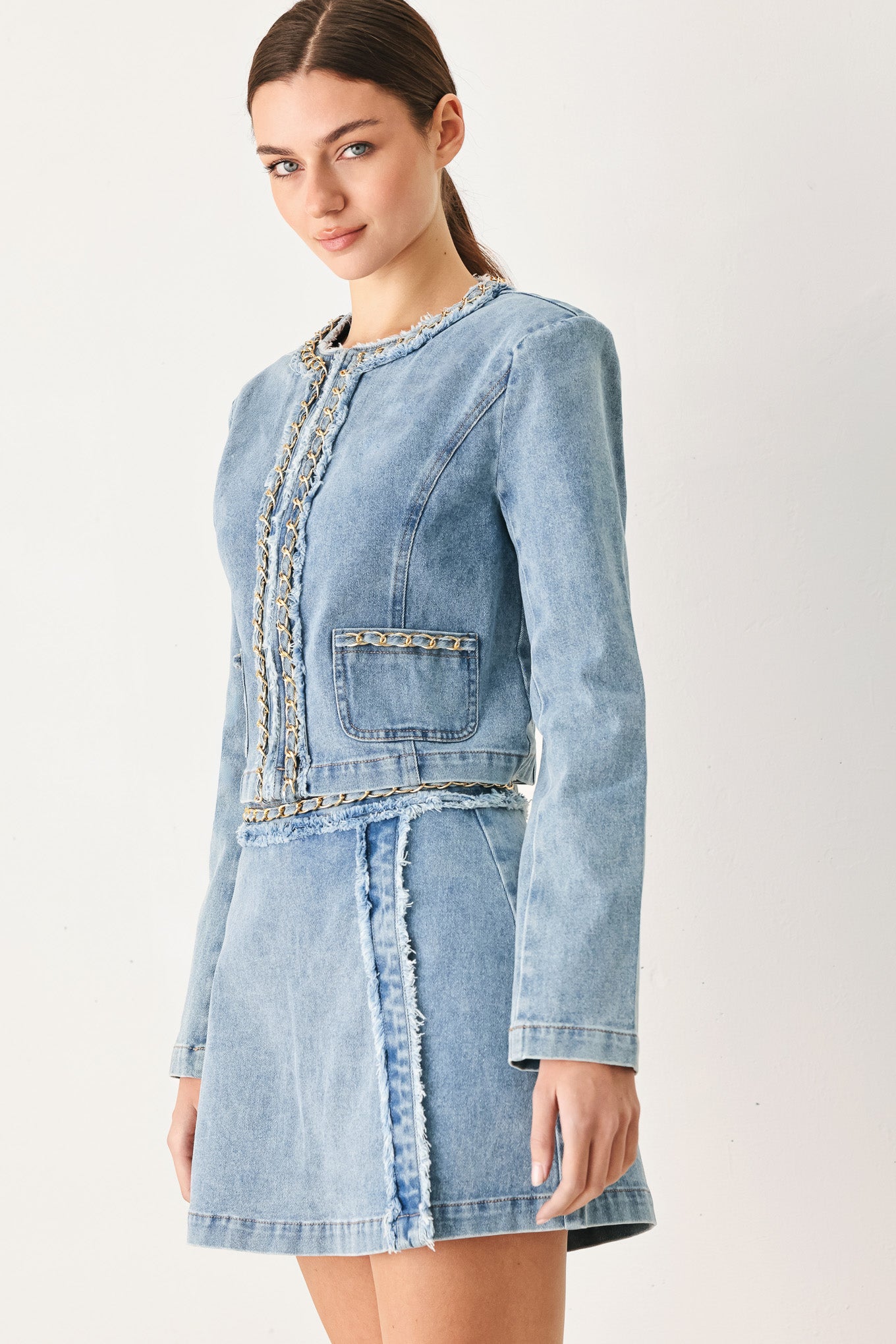 Woman wearing a light blue denim jacket featuring decorative gold chain trim and frayed details | FREEMARKET