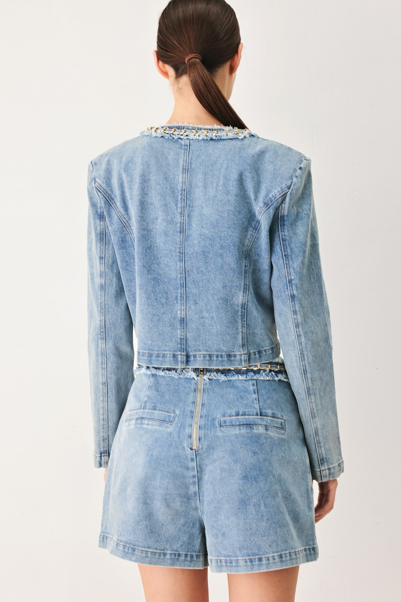 Woman wearing a light blue denim jacket featuring decorative gold chain trim and frayed details | FREEMARKET