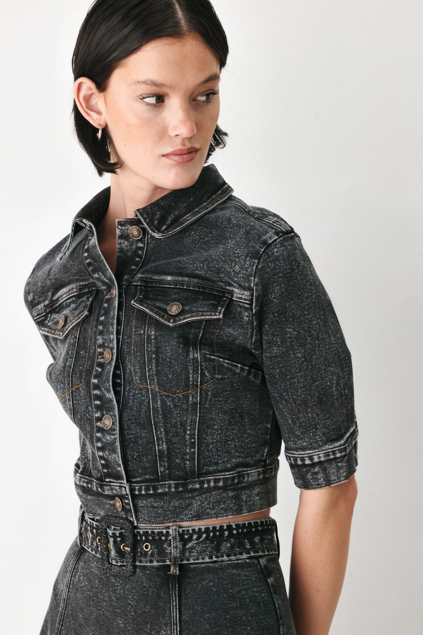 A model wearing a cropped, short-sleeved black acid-wash denim jacket with a band collar and button front | FREEMARKET